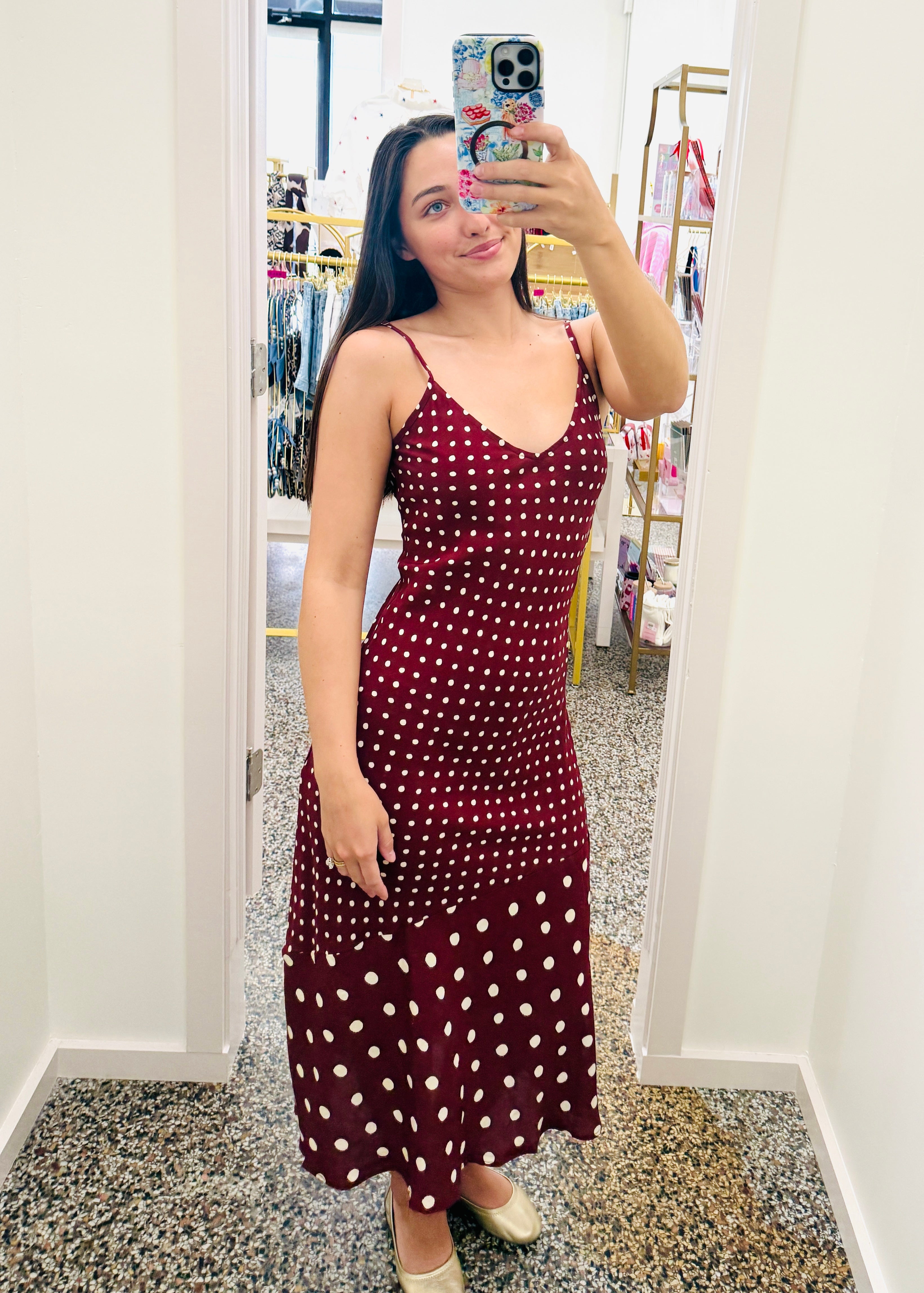 Woman taking a mirror selfie wearing a burgundy dress with white polka dots in a store.