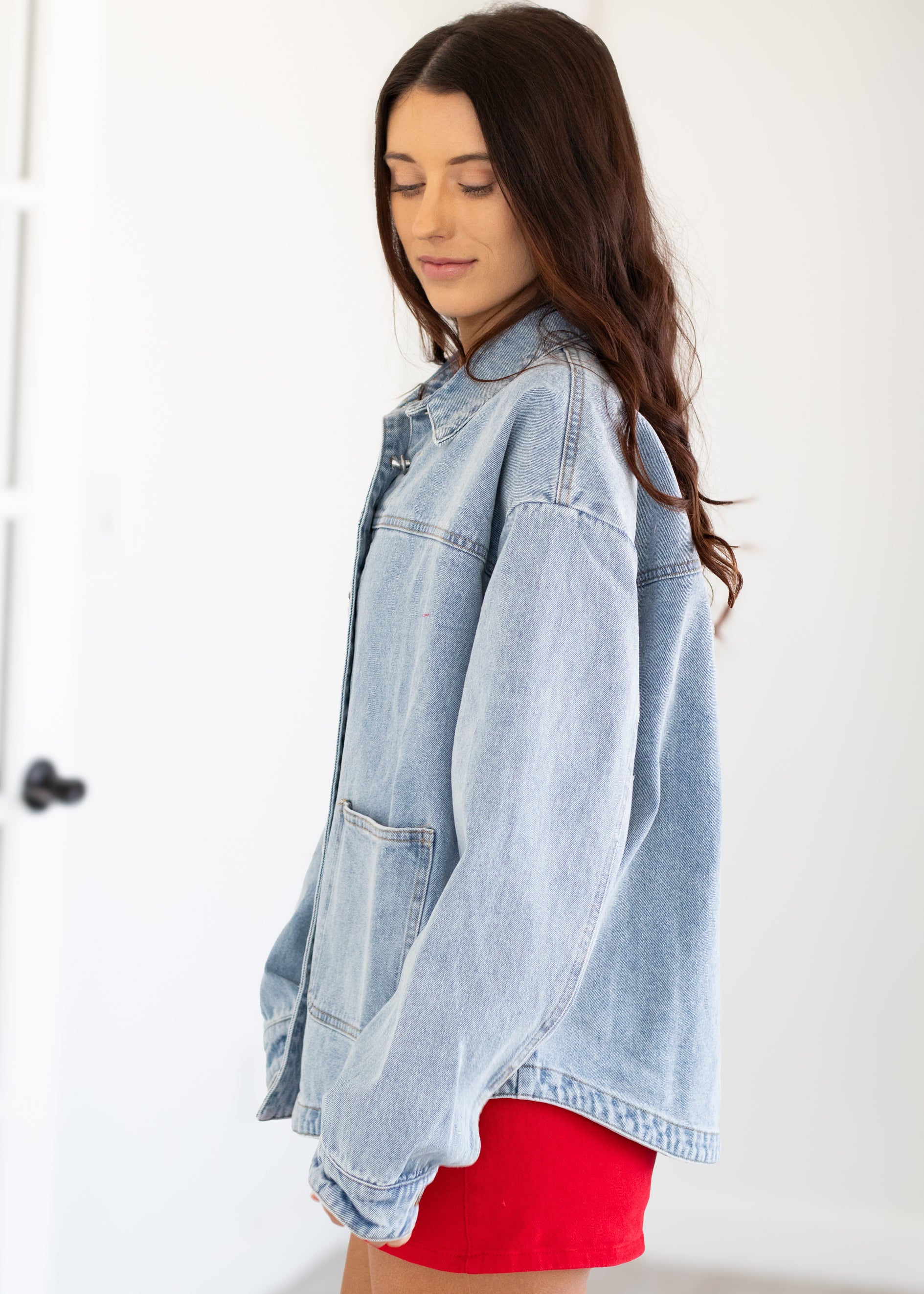 Woman wearing a light blue denim jacket over a red outfit on a white background