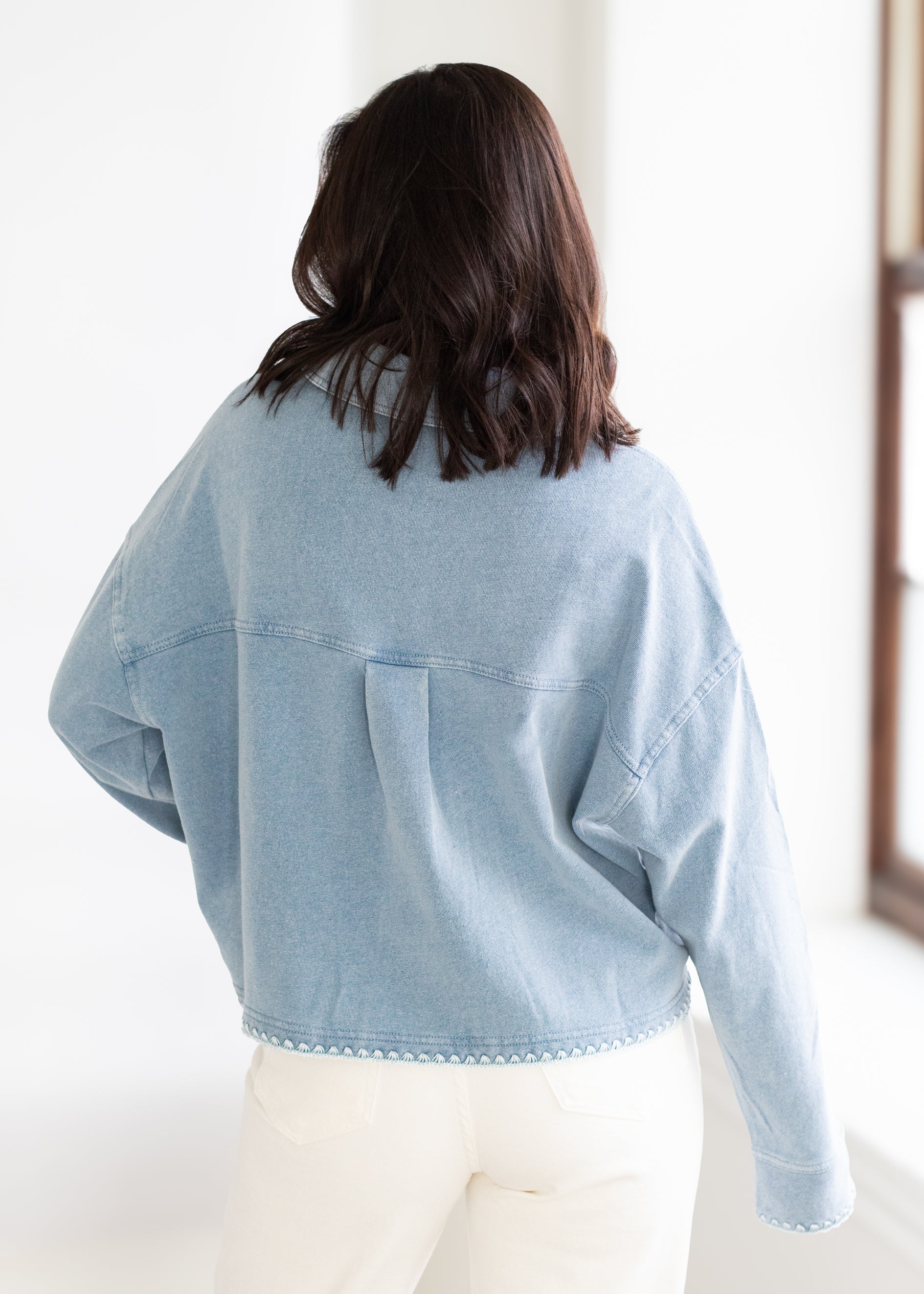 Person wearing a light blue denim jacket in a minimal indoor setting