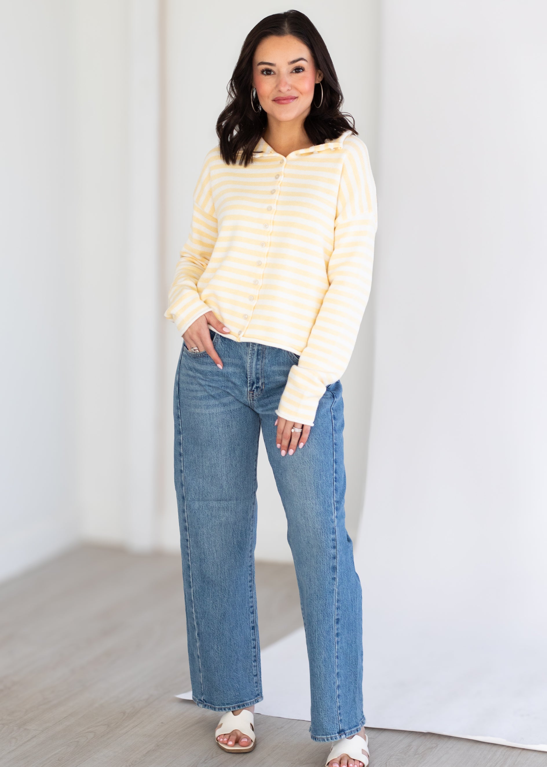 Woman wearing a yellow striped sweater and blue jeans against a white background