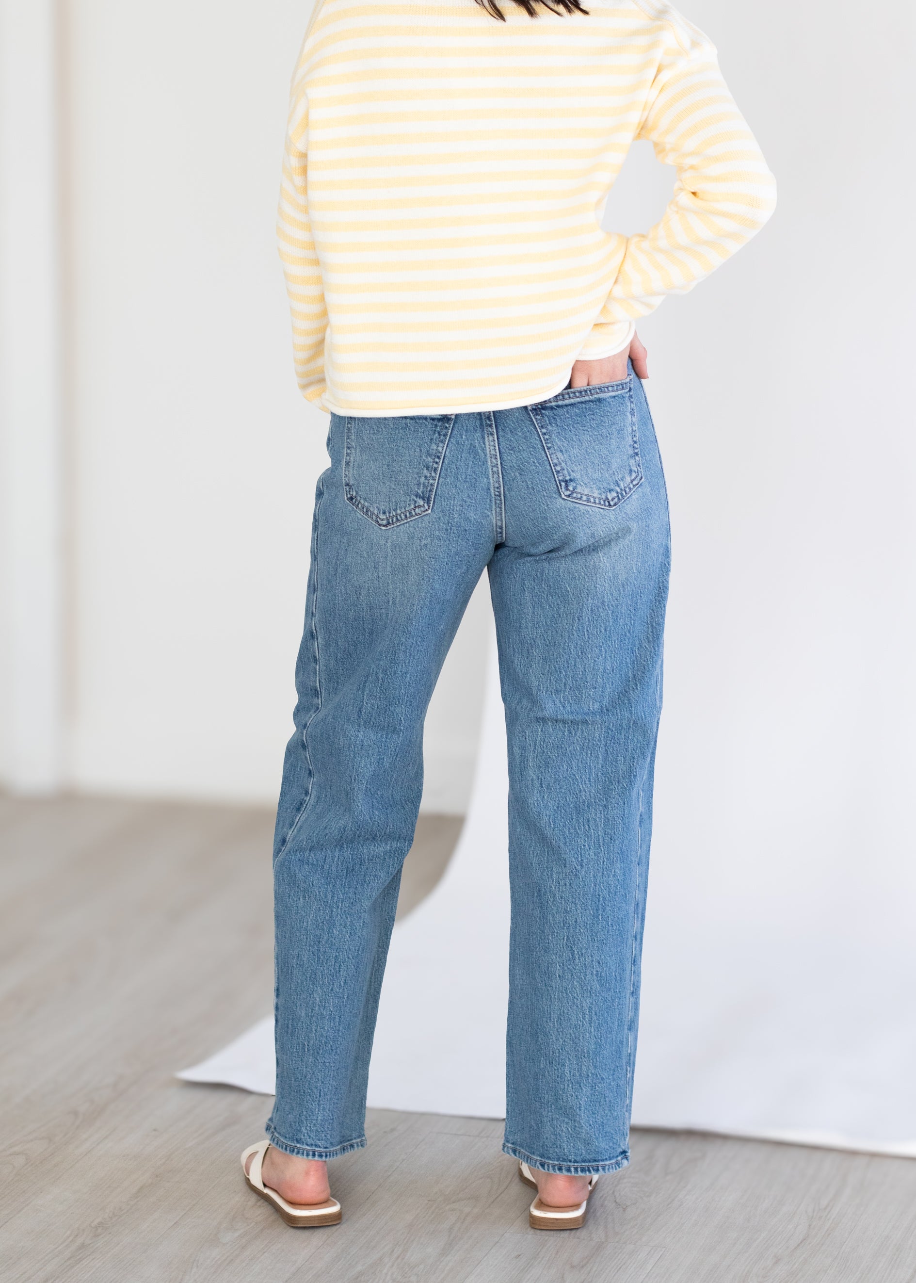 Person wearing a yellow striped sweater and blue jeans on a plain background