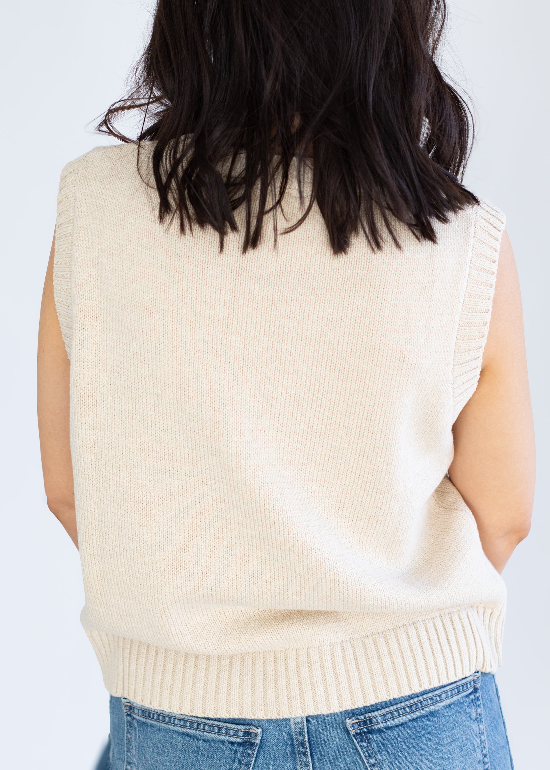 Person wearing a beige knitted vest over a blue top on a plain background