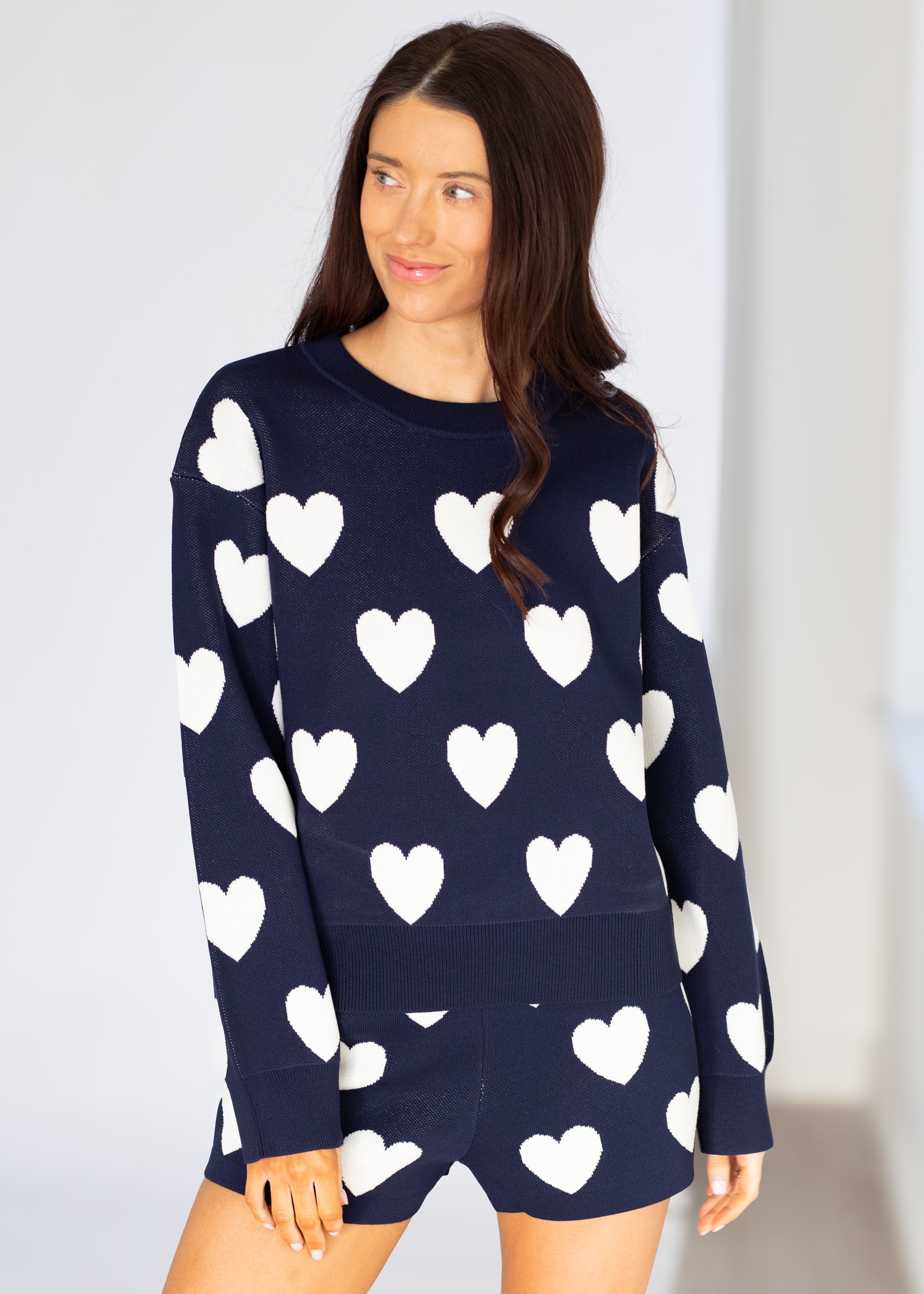 Woman wearing a navy sweater with white heart patterns on a plain background