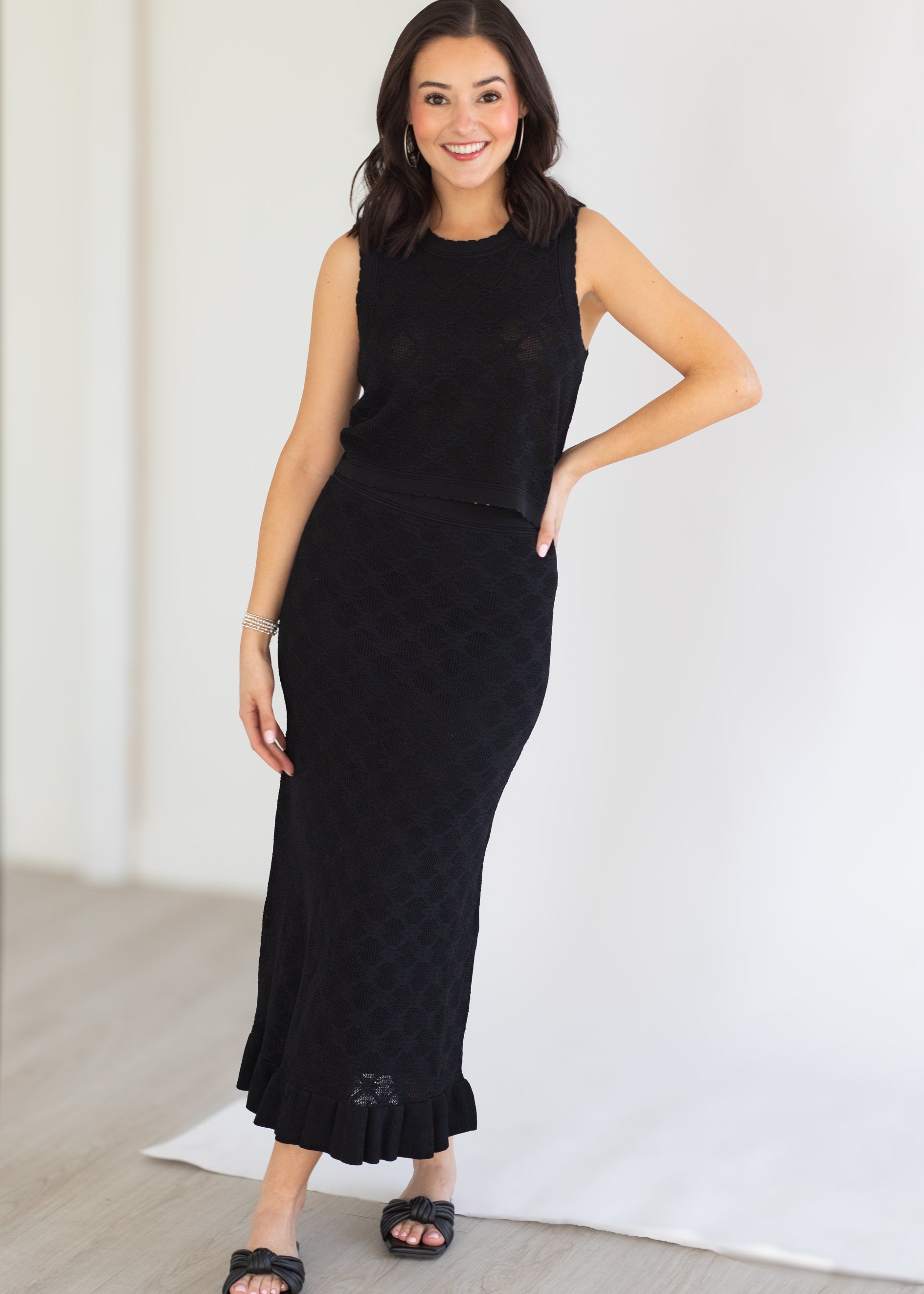 Woman wearing a black sleeveless top and quilted skirt against a white background