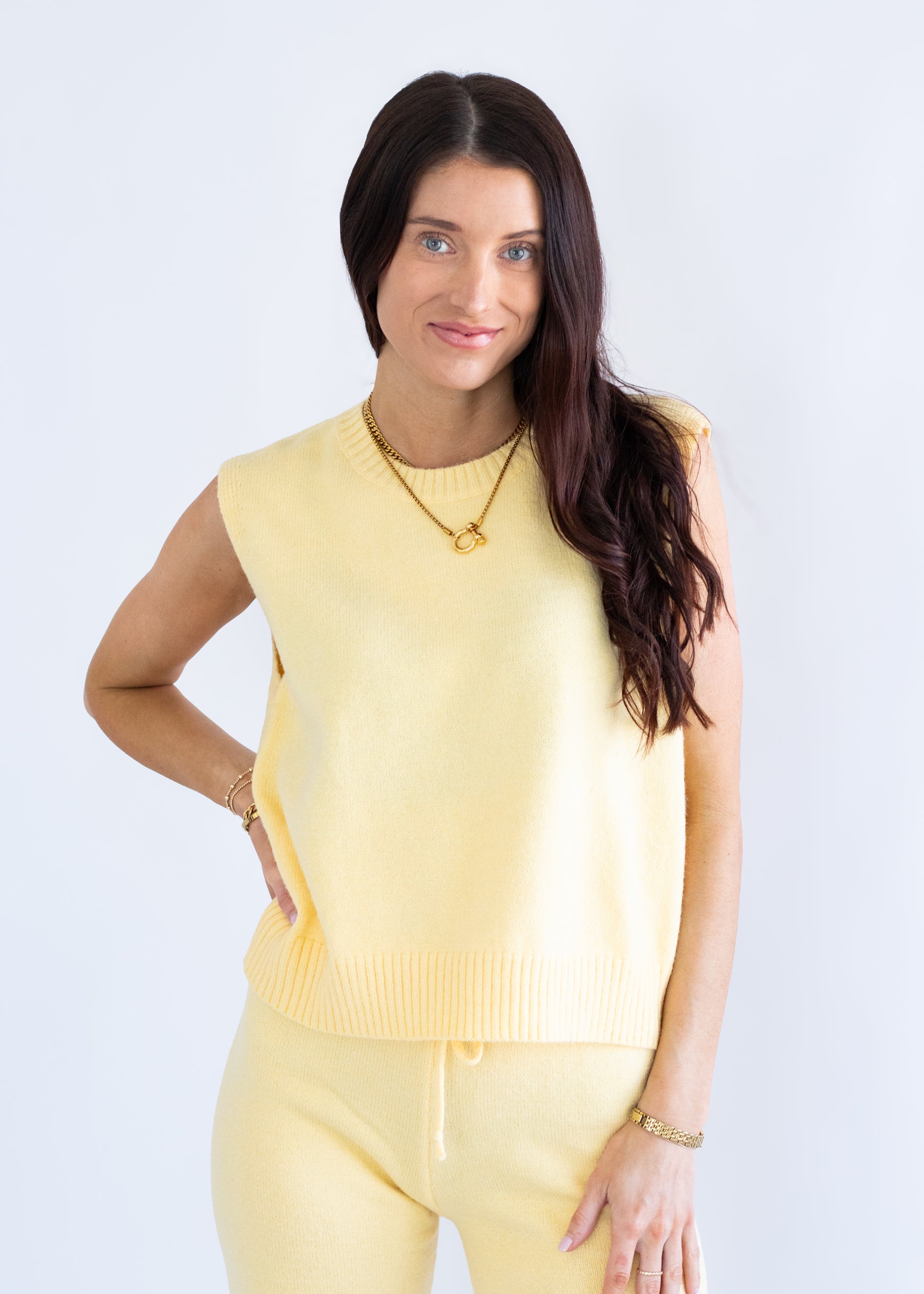 Woman wearing a yellow sleeveless top and pants on a light gray background