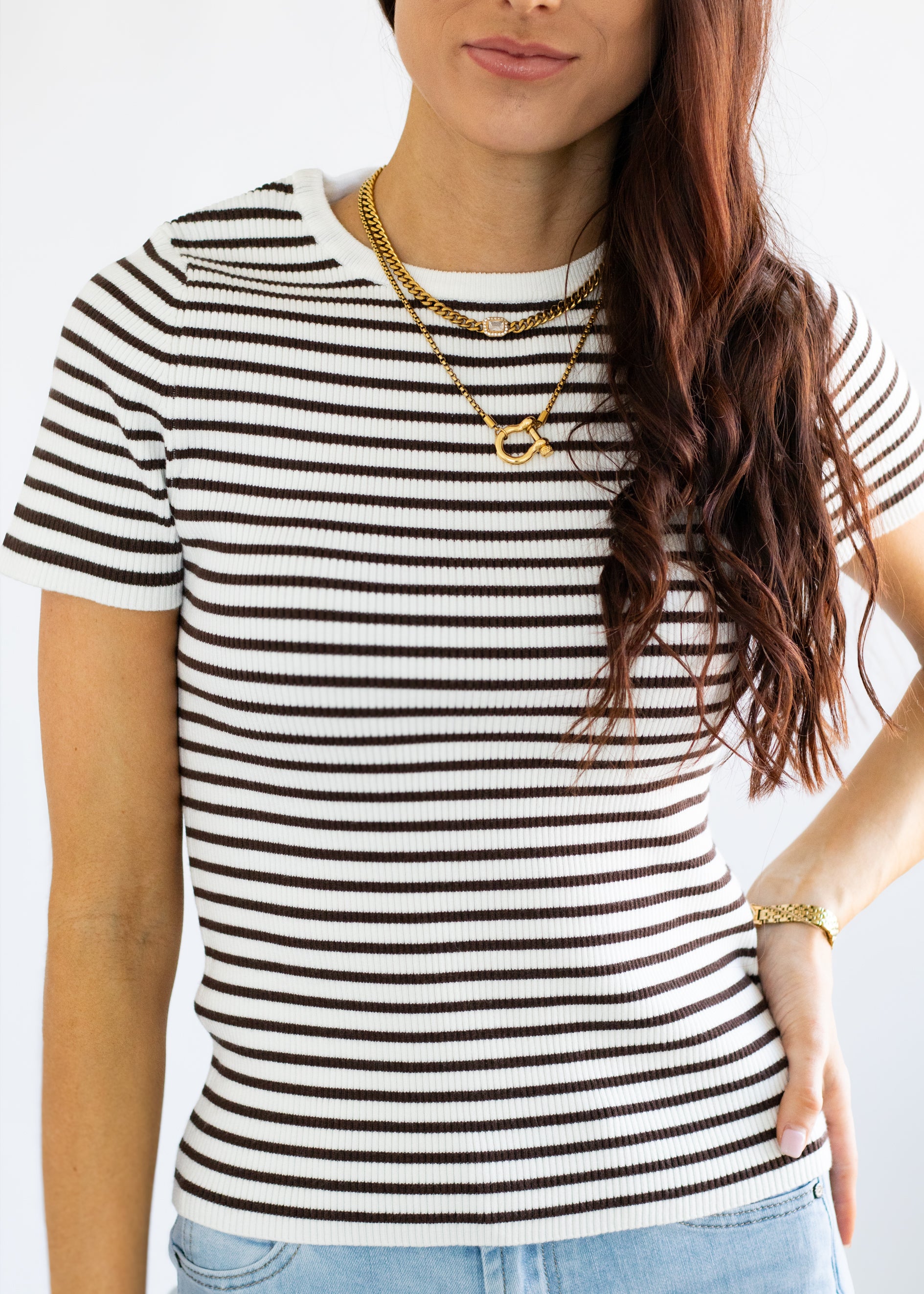 Woman wearing a black and white striped shirt with layered gold necklaces.
