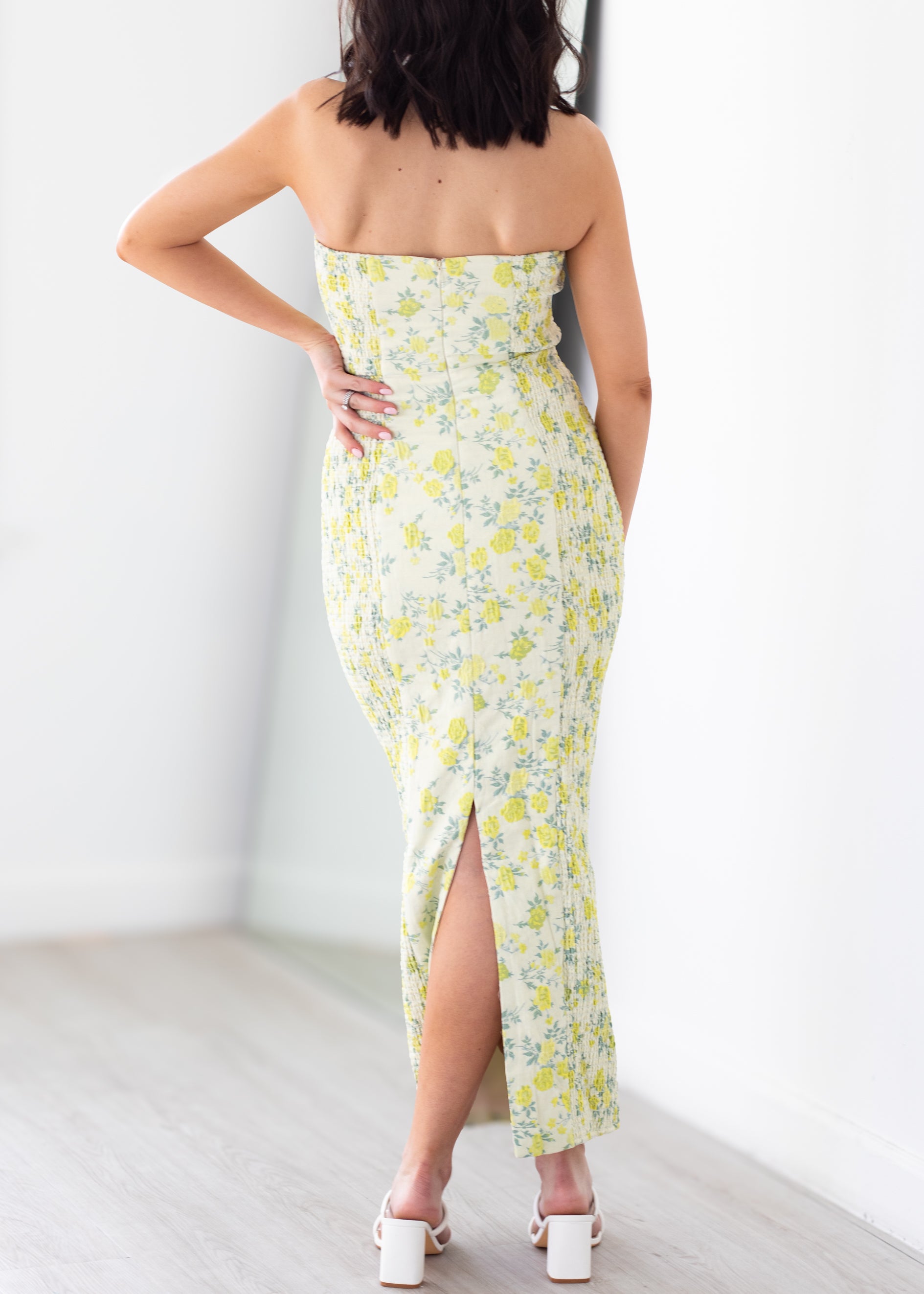 Woman wearing a strapless floral dress with a slit on a plain background