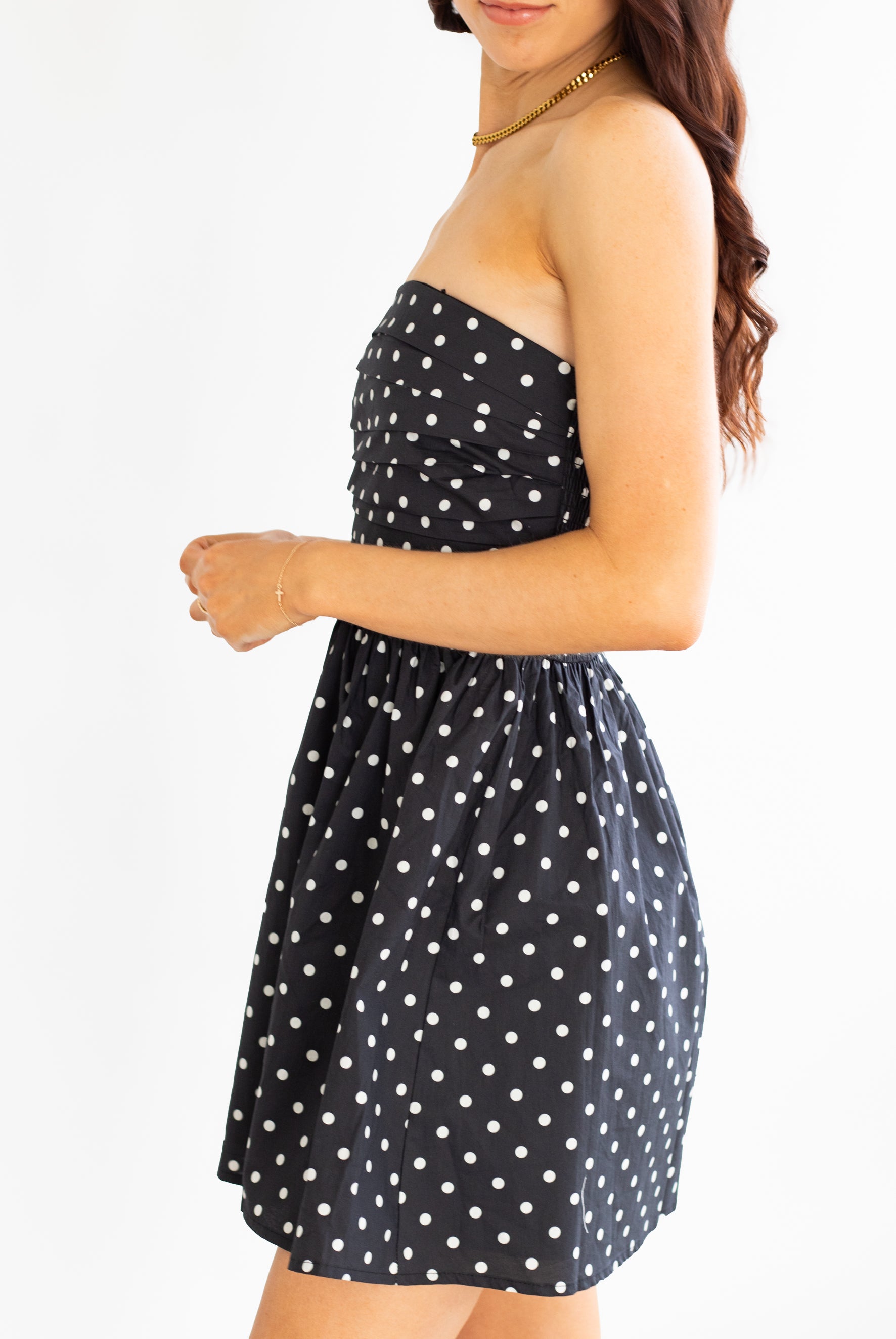 Woman wearing a black strapless dress with white polka dots on a white background