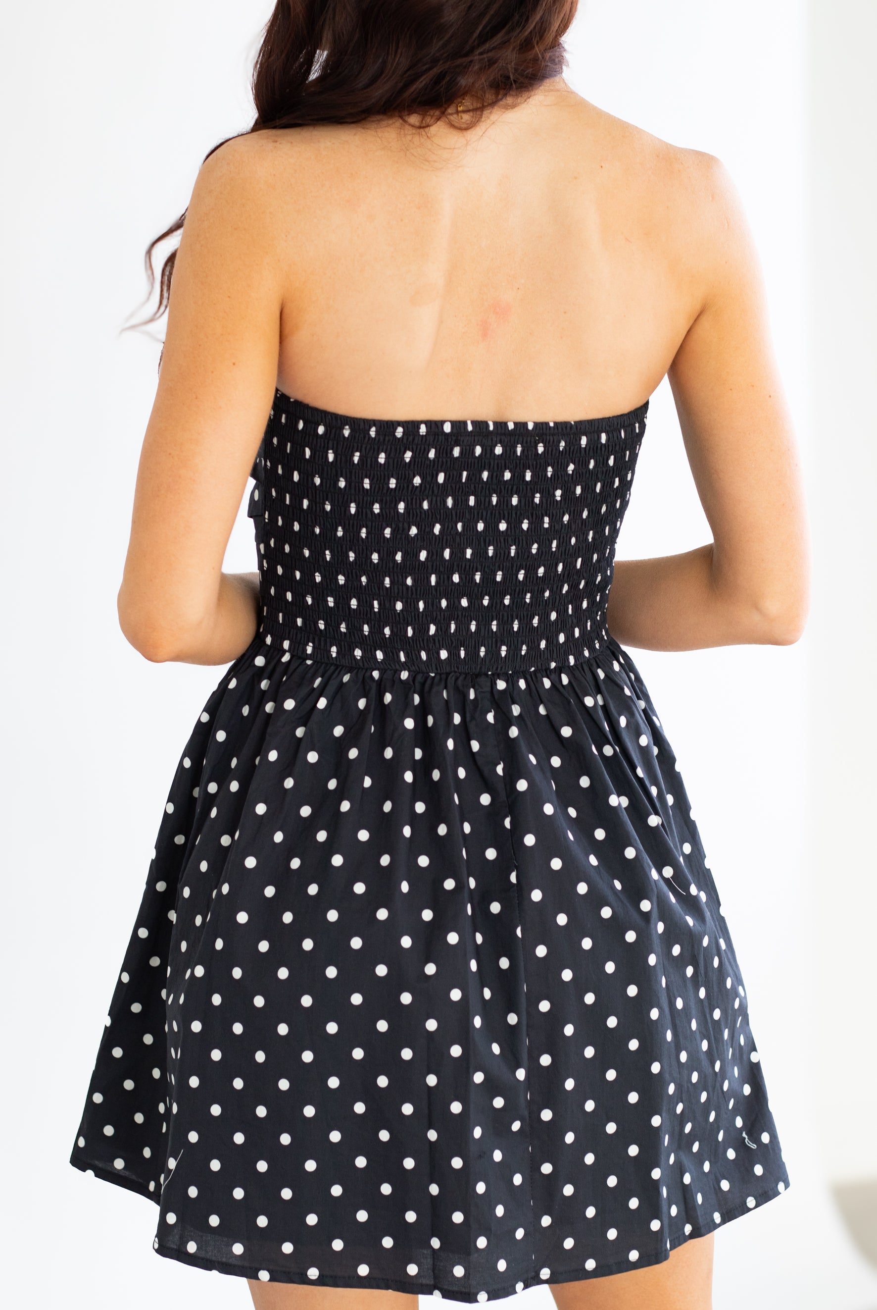 Black strapless dress with white polka dots on a plain background