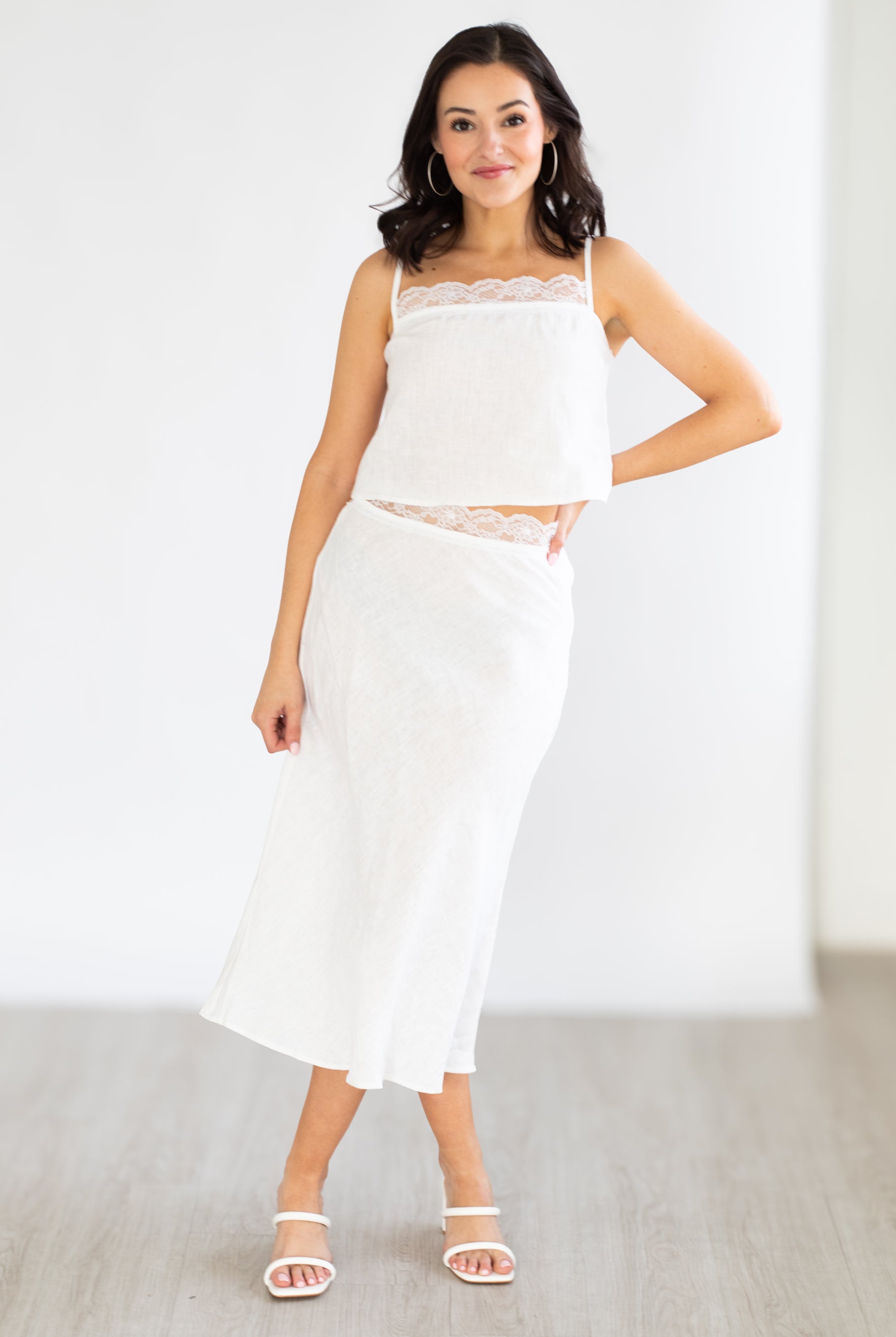 Woman wearing a white outfit with a lace top and skirt against a plain background