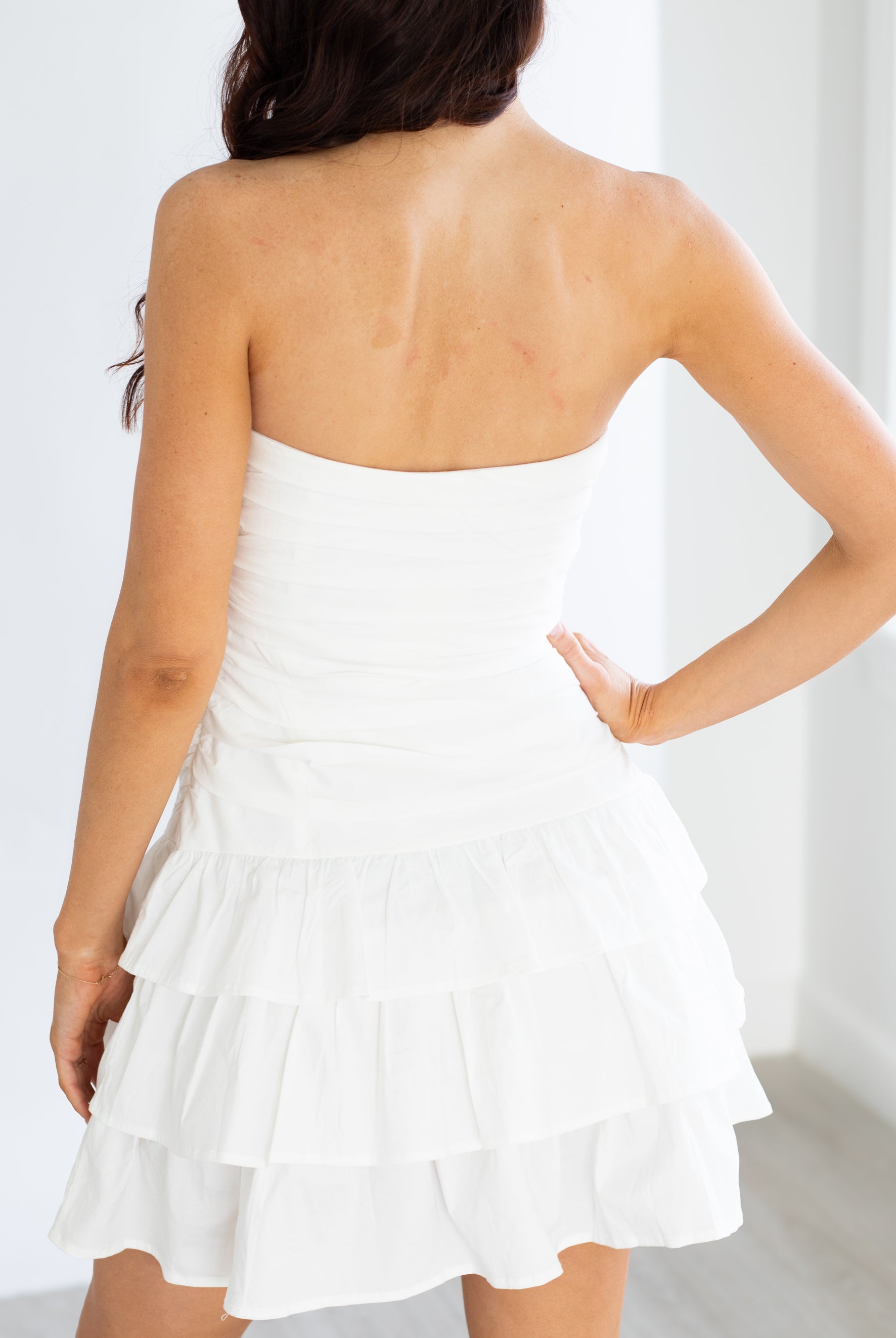 Woman wearing a white strapless dress with ruffled layers against a white background