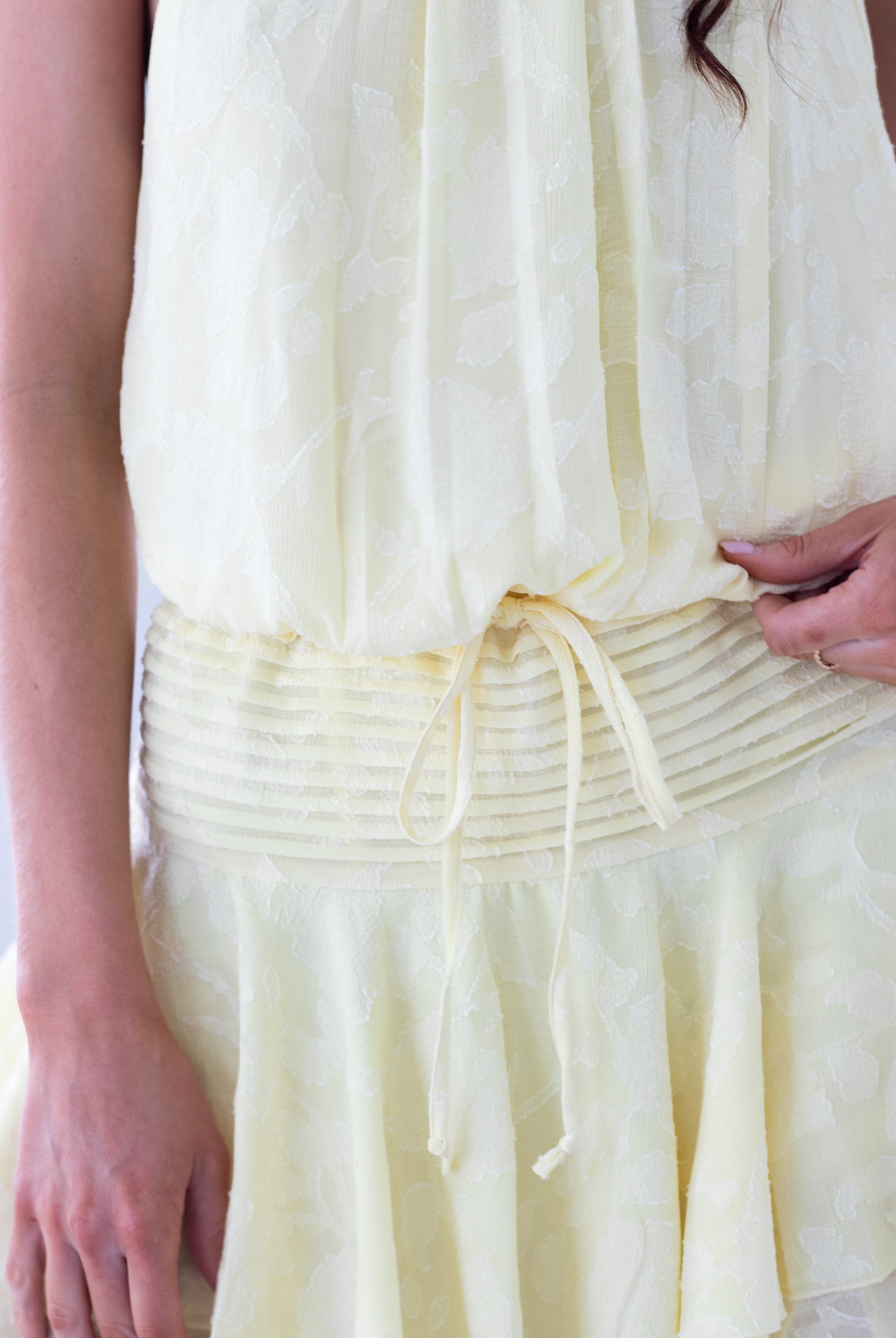 Close-up of a person wearing a light yellow dress with a white background