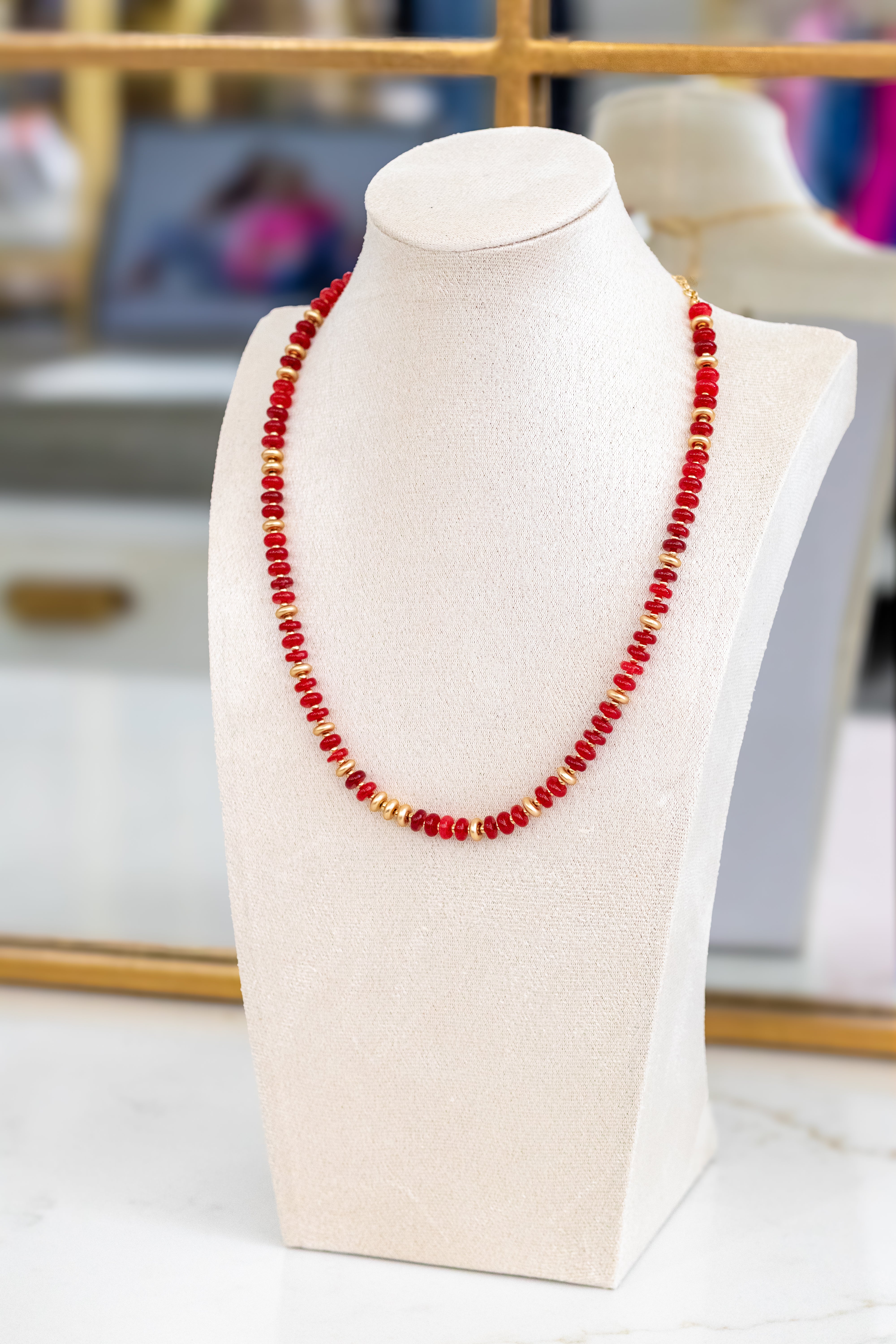 Red beaded necklace on a white mannequin bust with a blurred background