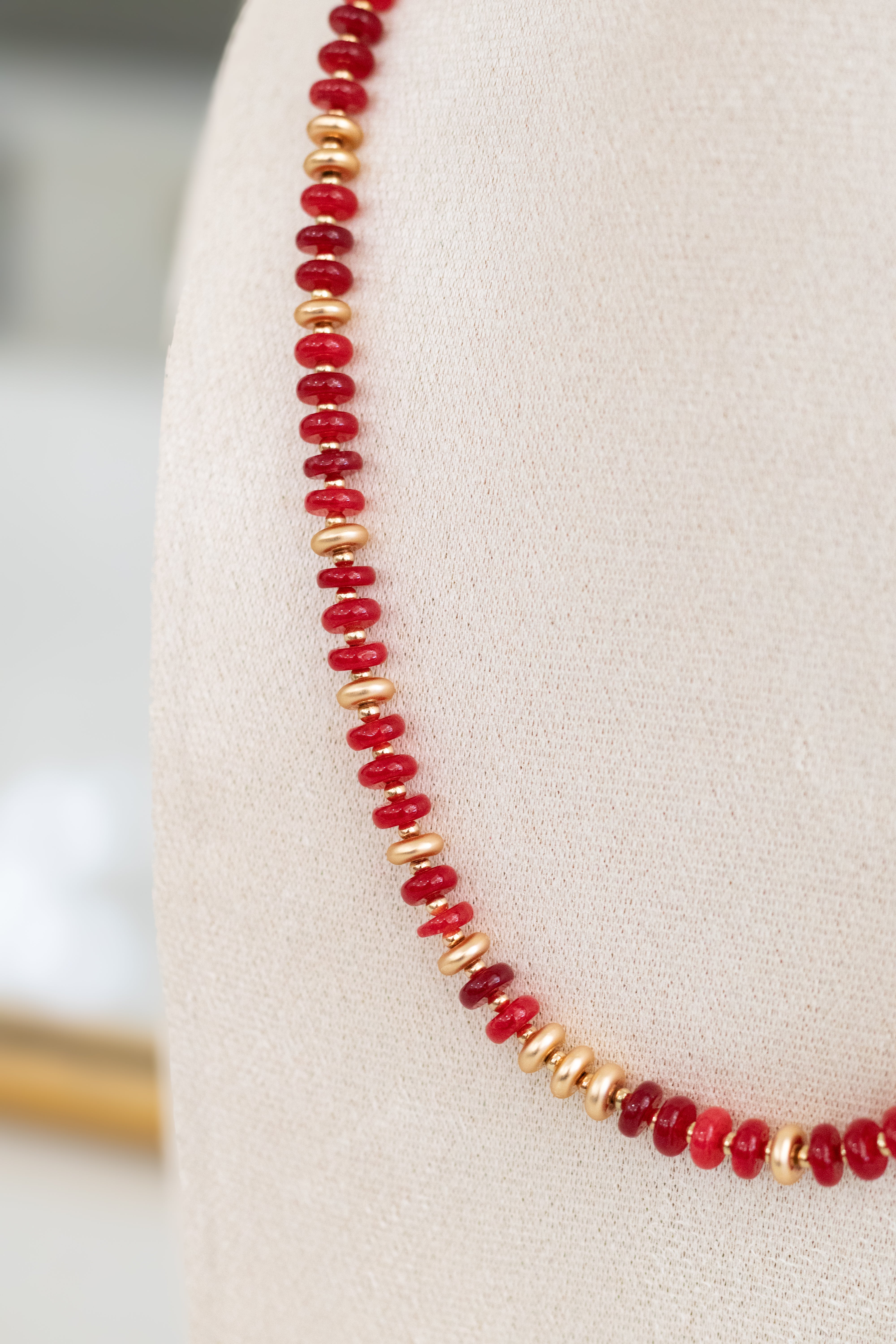 Necklace with red and gold beads on a white cushion