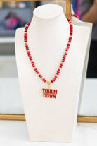 Red beaded necklace with 'TOUCHDOWN' pendant on a white bust