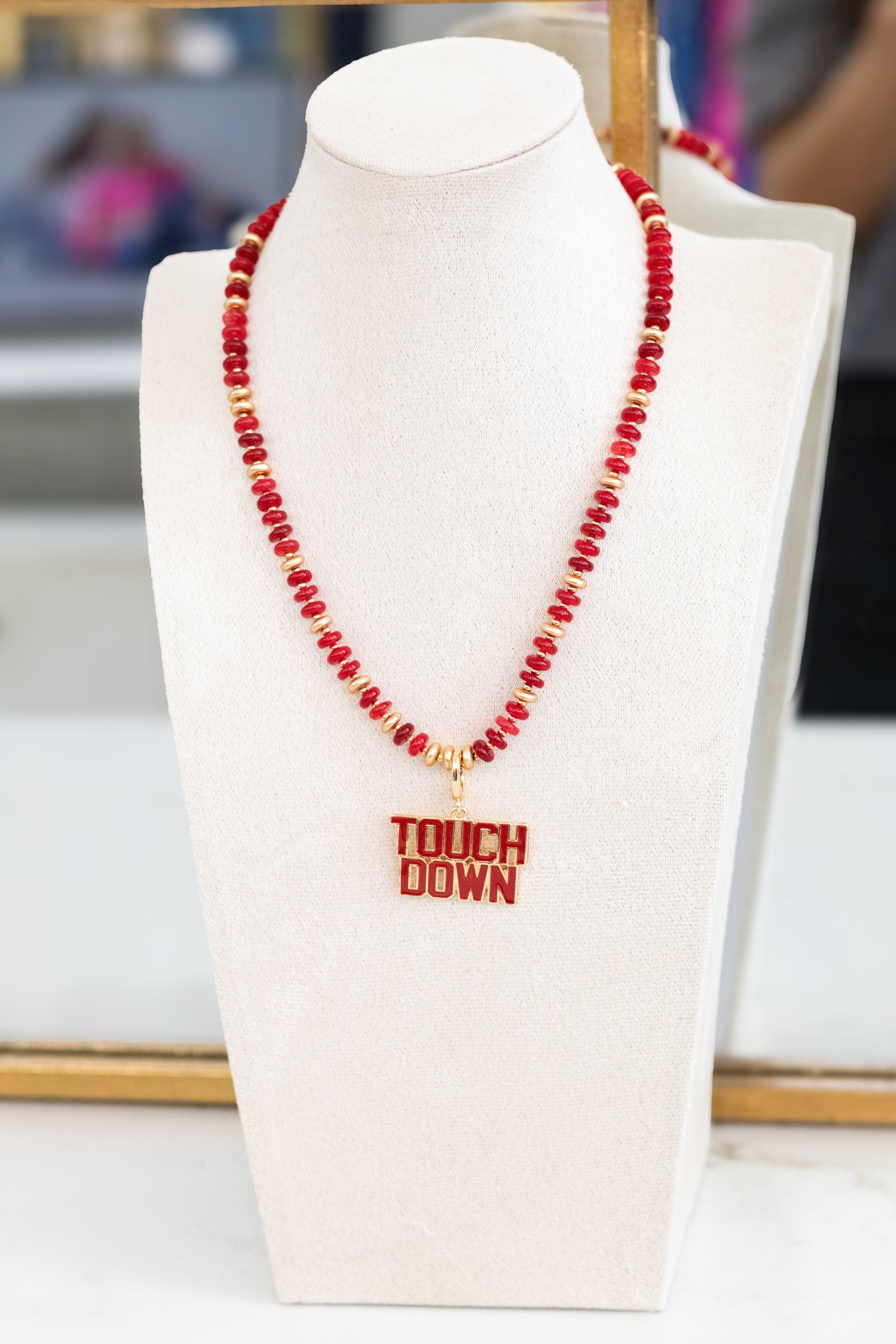 Red beaded necklace with 'TOUCHDOWN' pendant on a white bust