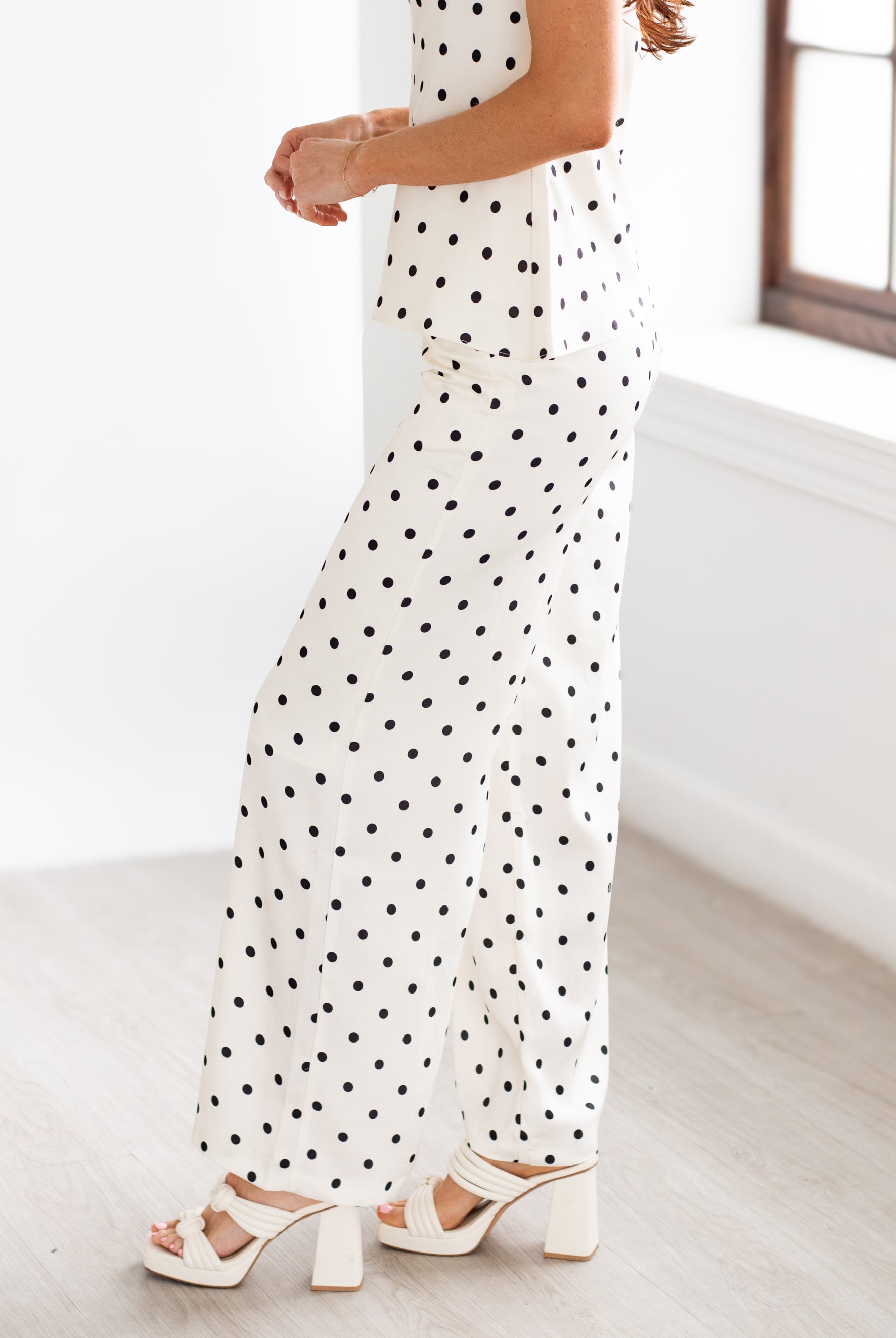 Woman wearing a polka dot dress with white sandals in a minimal indoor setting