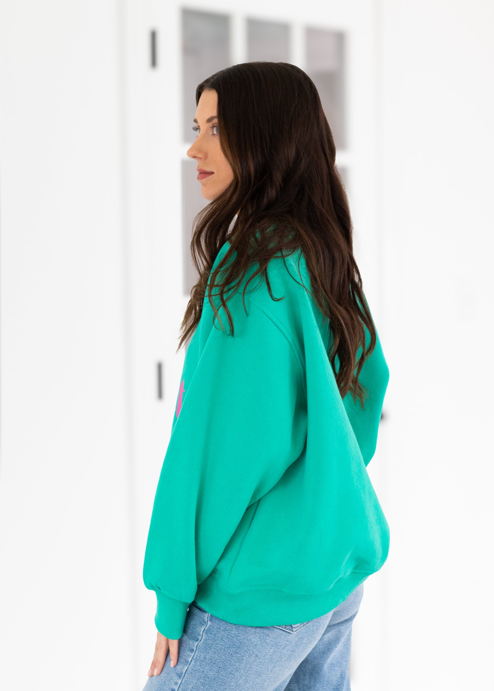 Woman wearing a teal sweatshirt in a minimal indoor setting