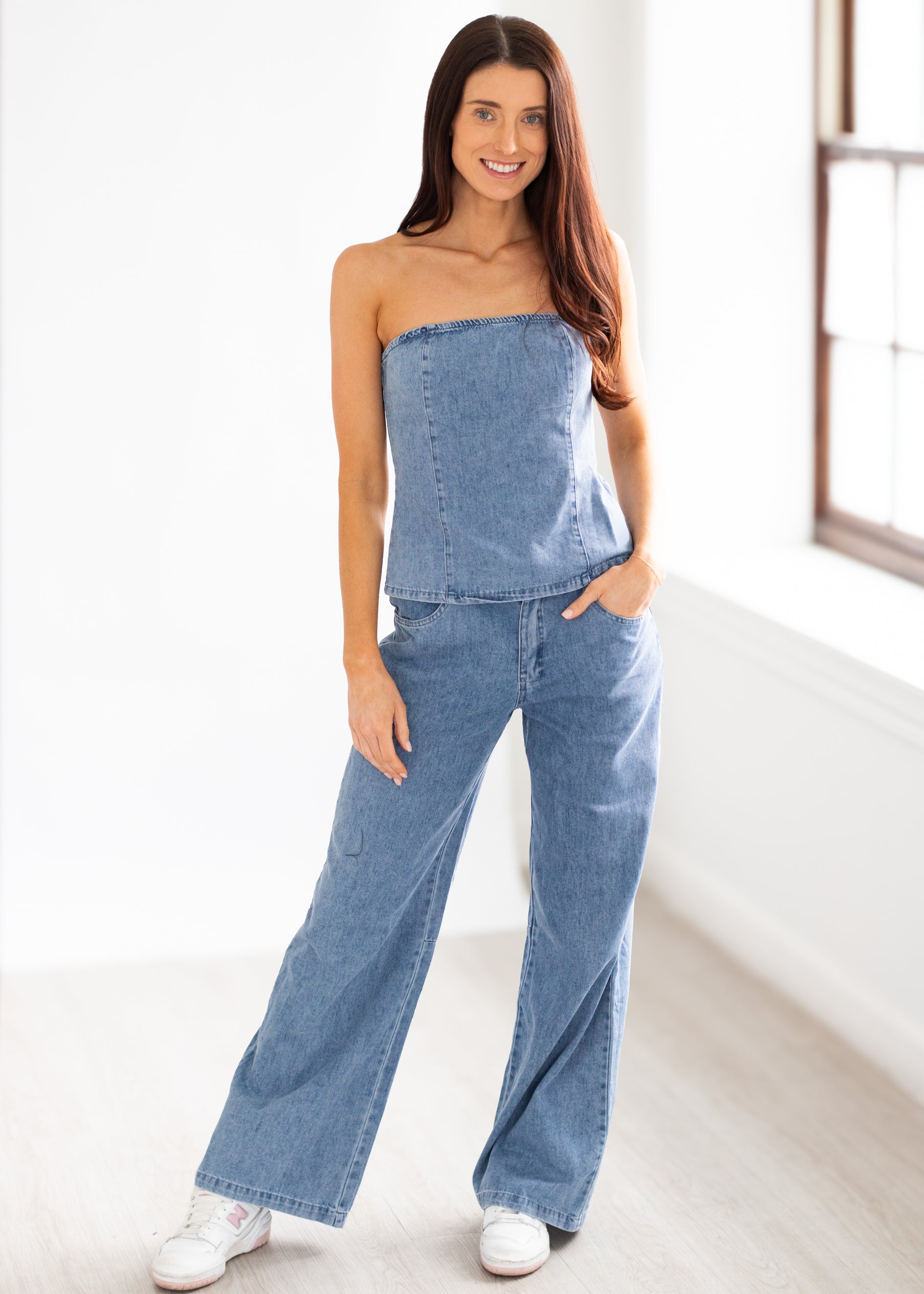 Woman wearing a denim strapless jumpsuit in a bright room.