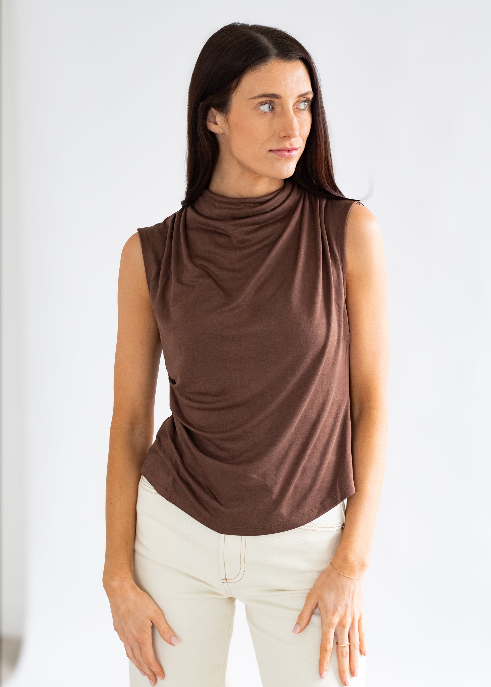 Woman wearing a brown sleeveless top and white pants against a plain background
