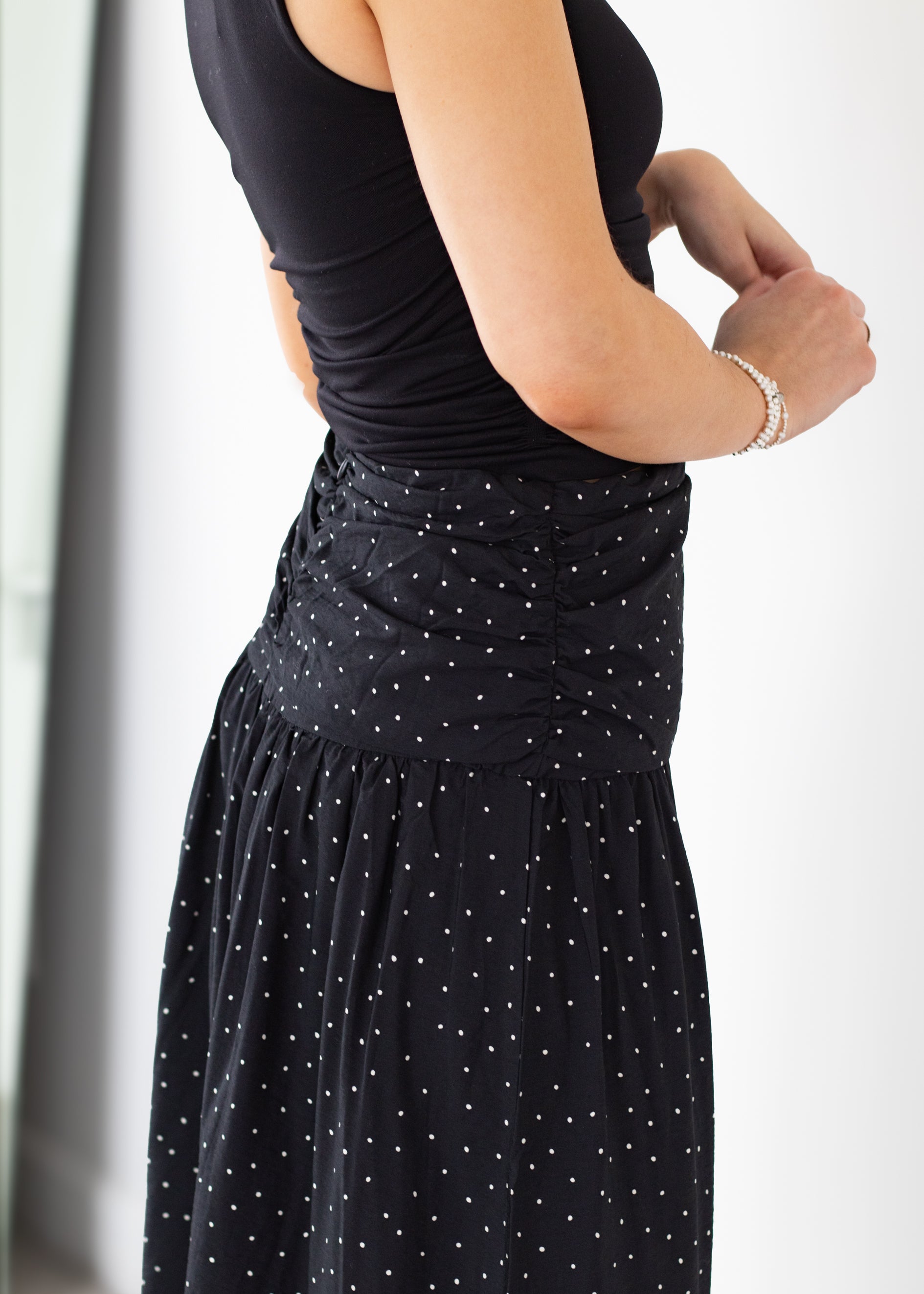 Person wearing a black sleeveless top and black polka dot skirt on a white background