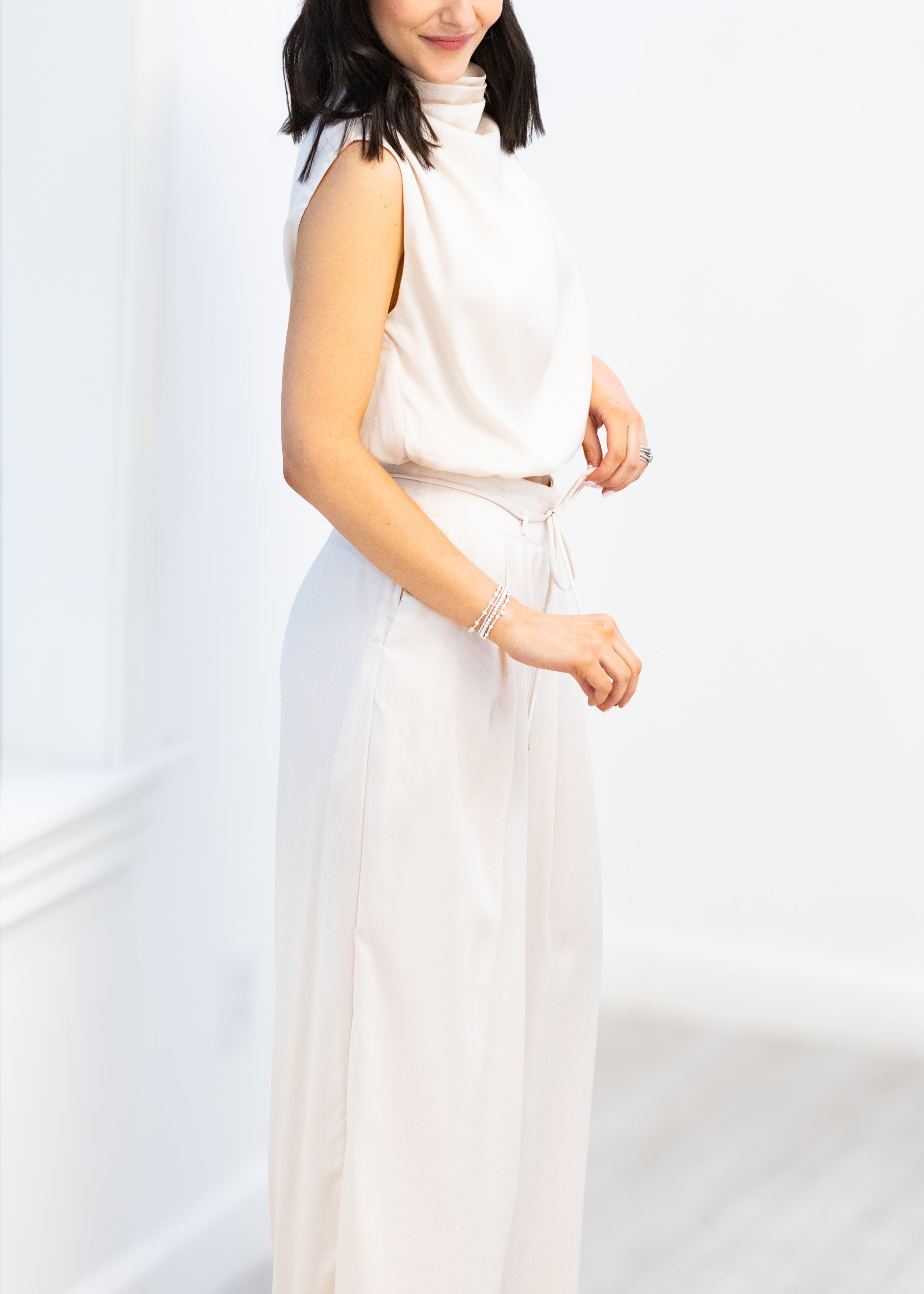 Woman wearing a white sleeveless top and pants against a white background