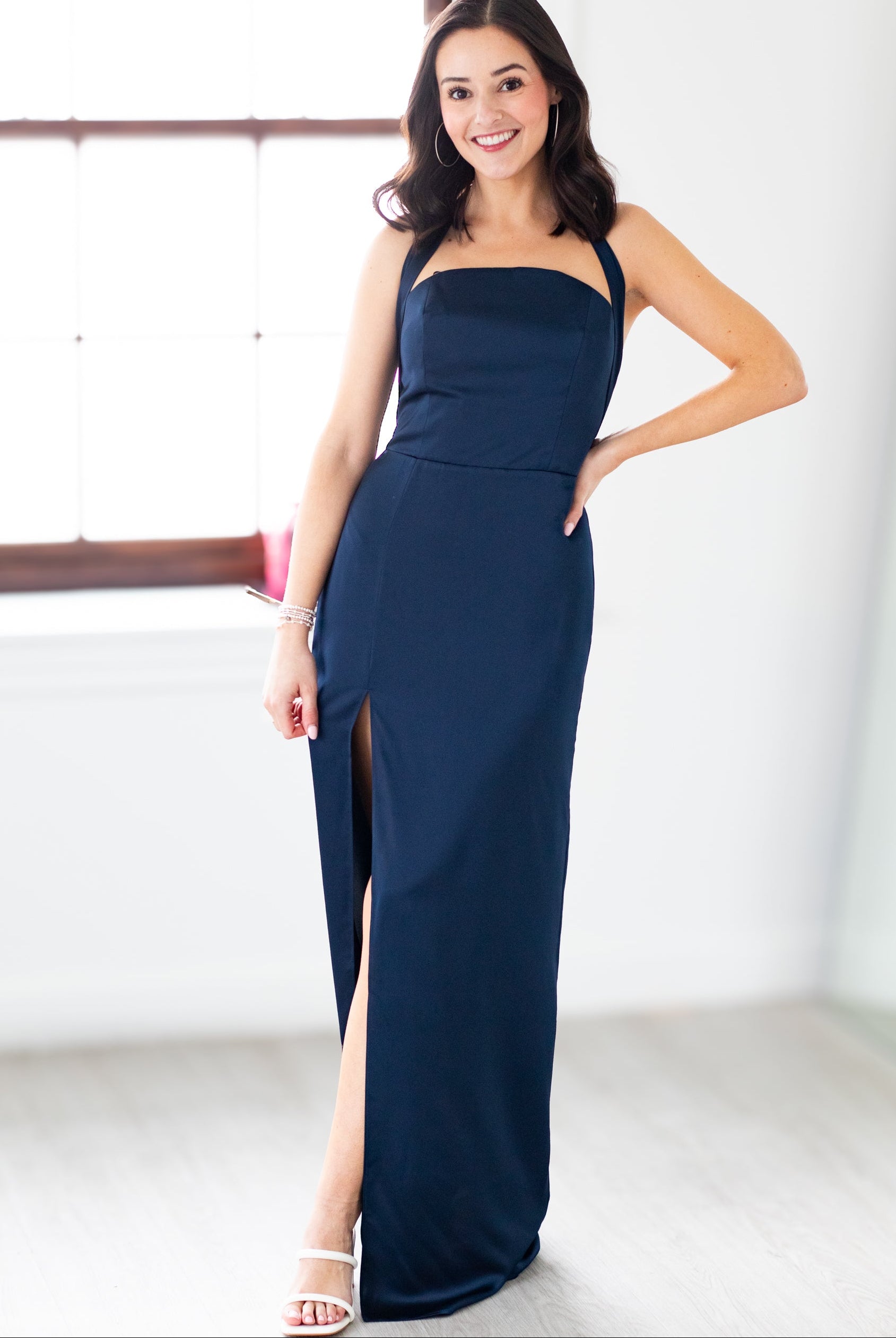 Woman wearing a navy blue evening gown with a slit, standing indoors.