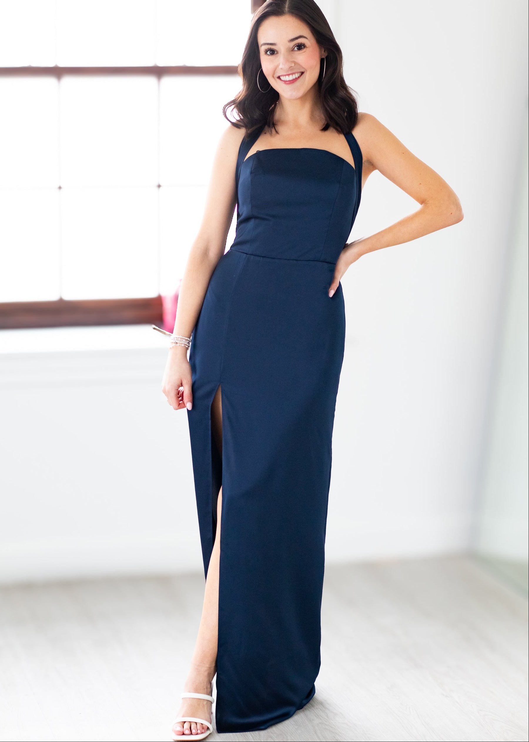 Woman wearing a navy blue evening gown with a slit, standing indoors.
