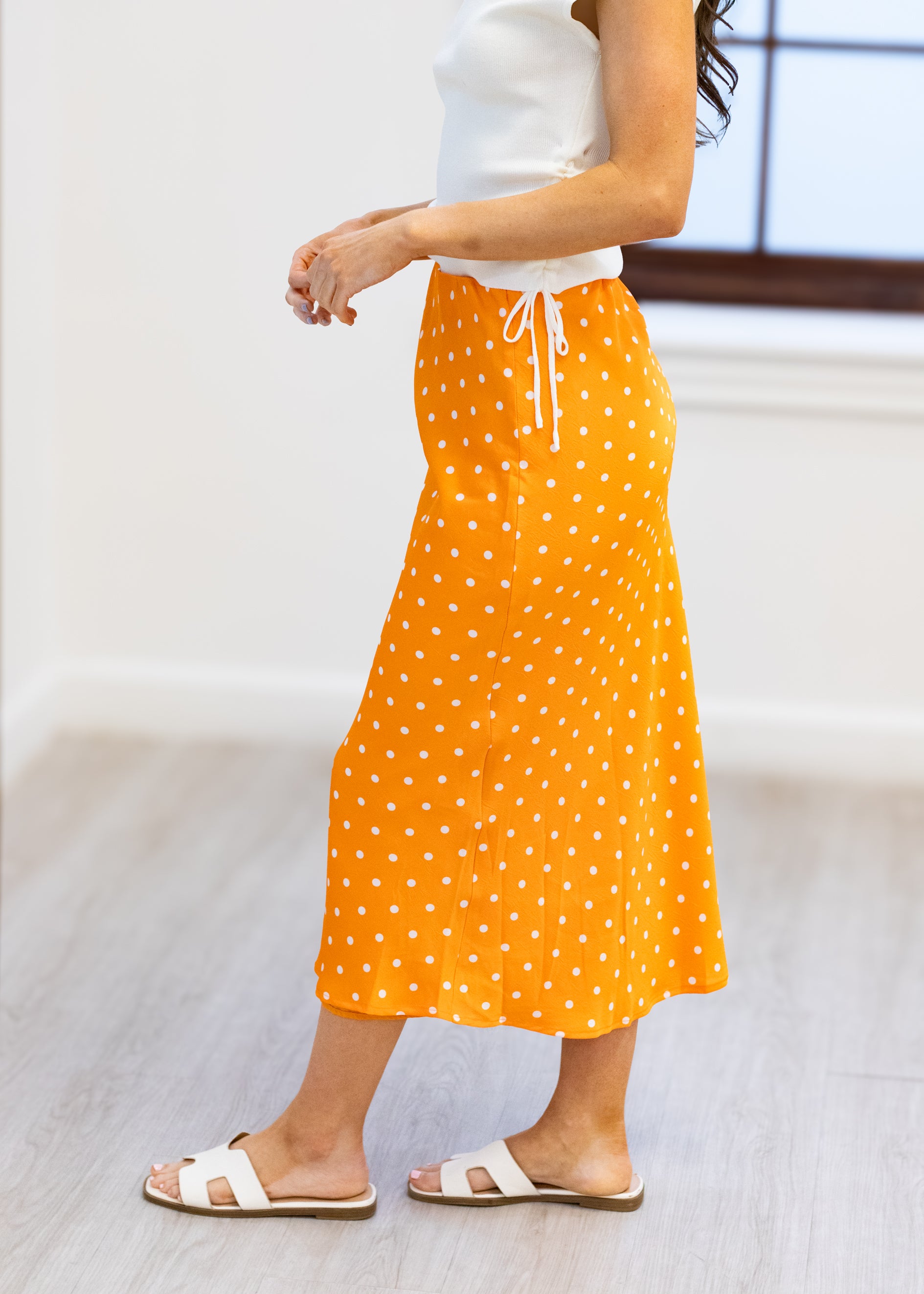 Person wearing an orange polka dot skirt with a white top on a light background