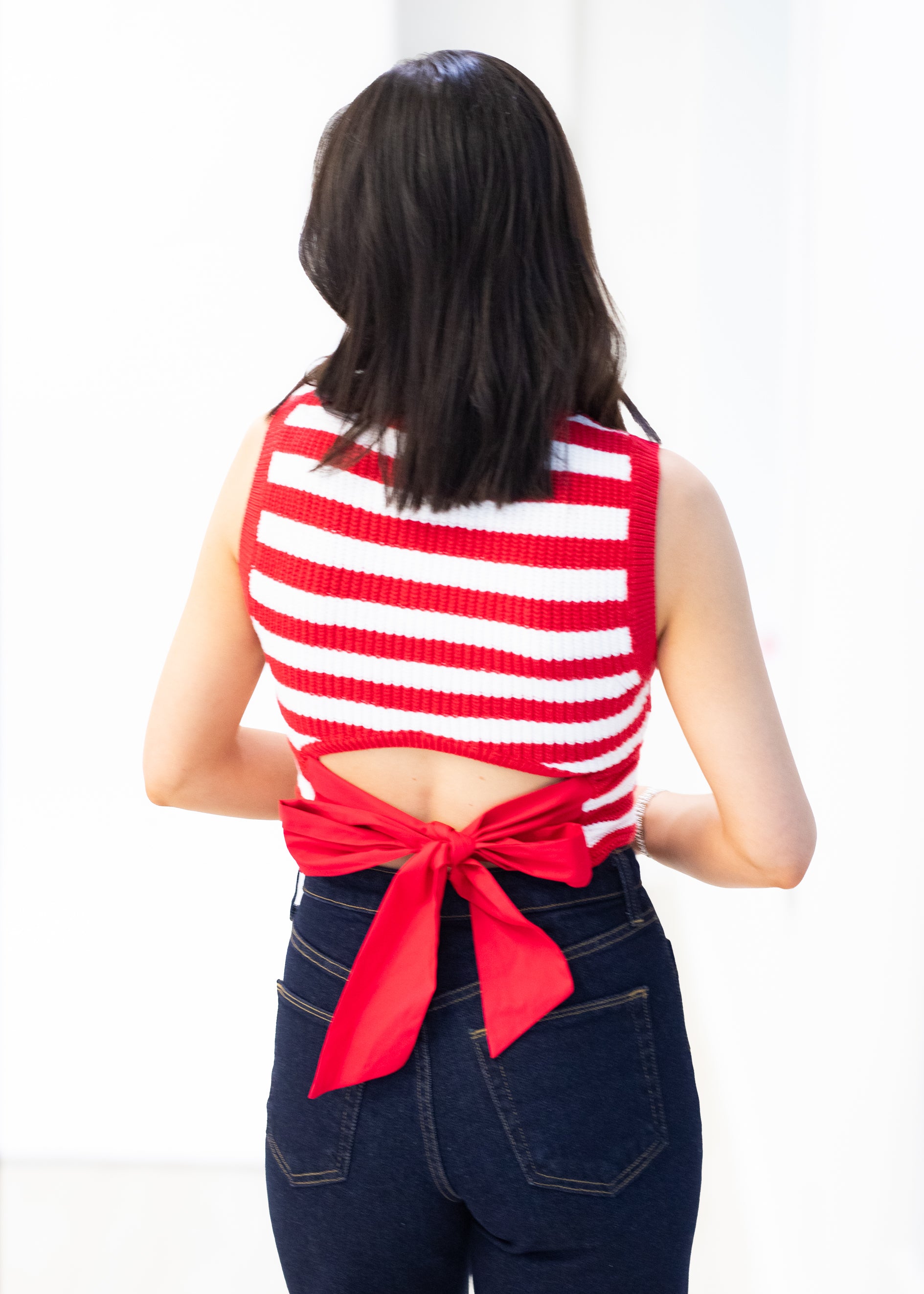 Person wearing a red and white striped sleeveless top with a bow detail on a white background