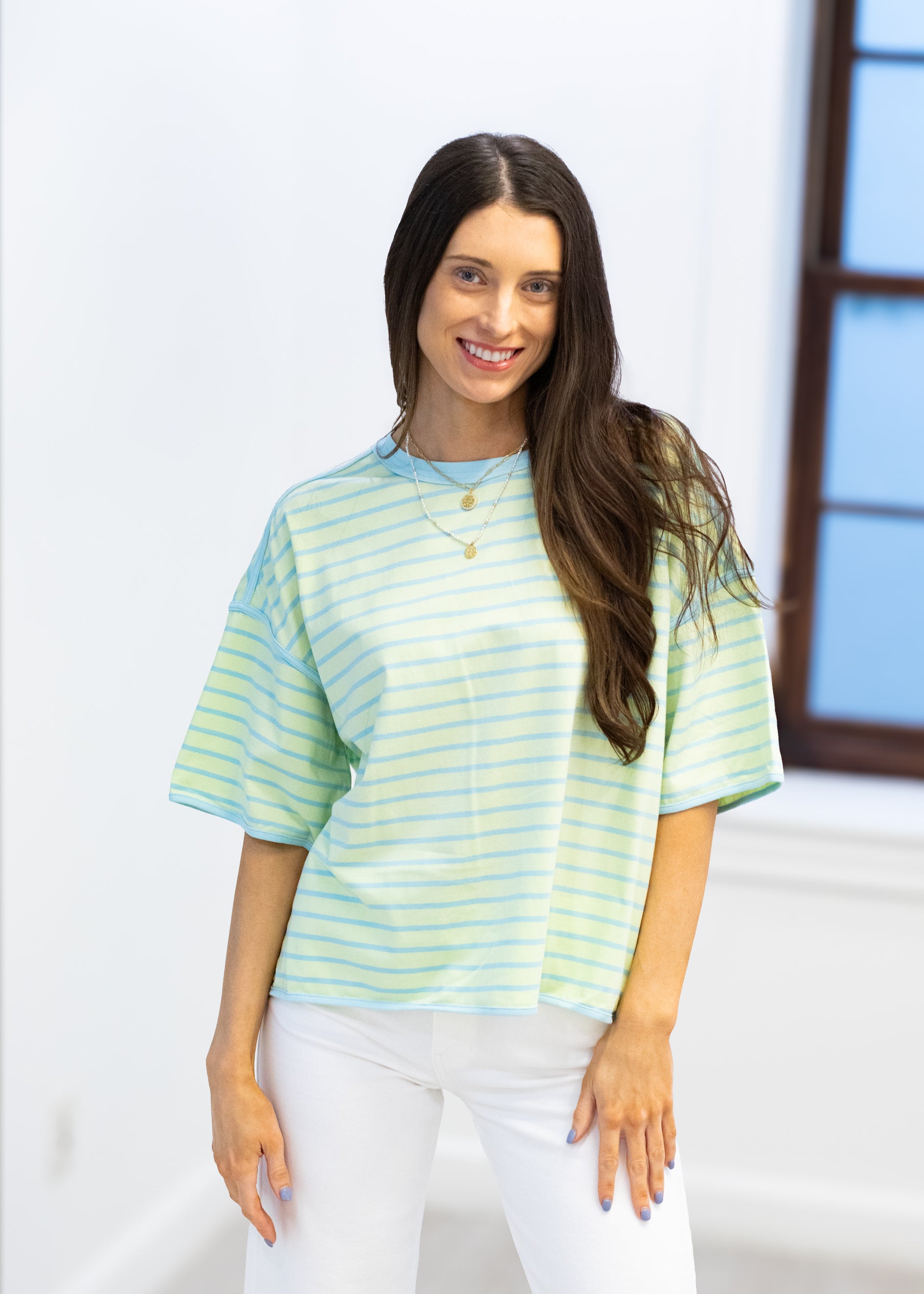 Woman wearing a light blue and yellow striped shirt with white pants against a white background
