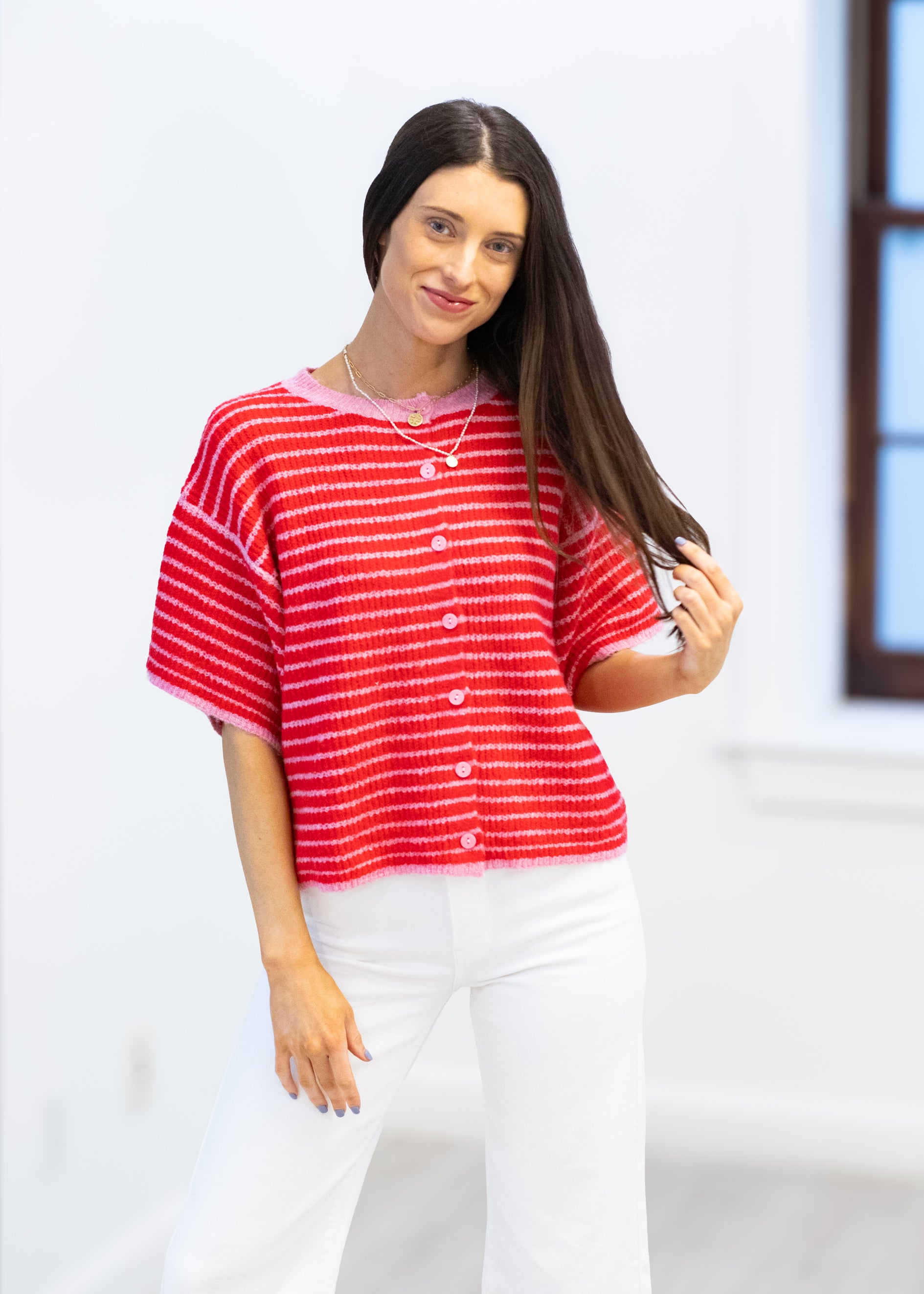 Woman wearing a red and white striped shirt and white pants against a light background