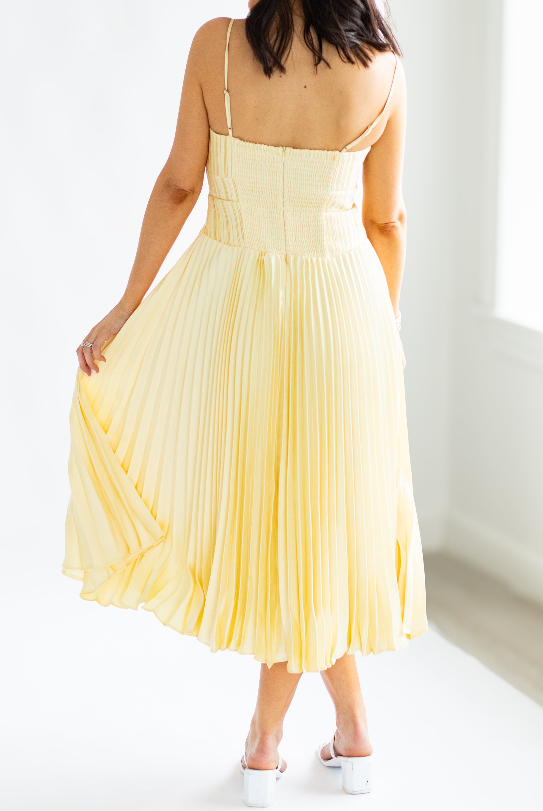 Woman wearing a yellow pleated dress against a white background