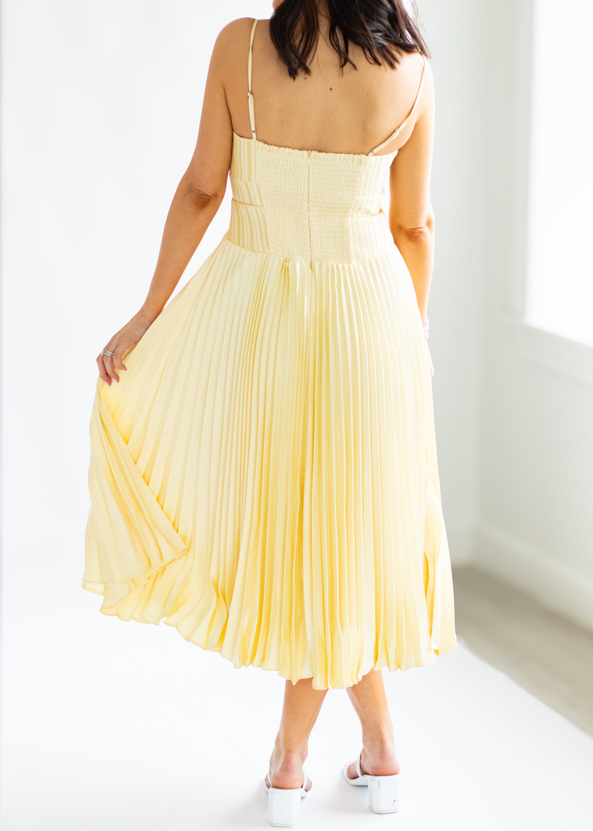 Woman wearing a yellow pleated dress against a white background