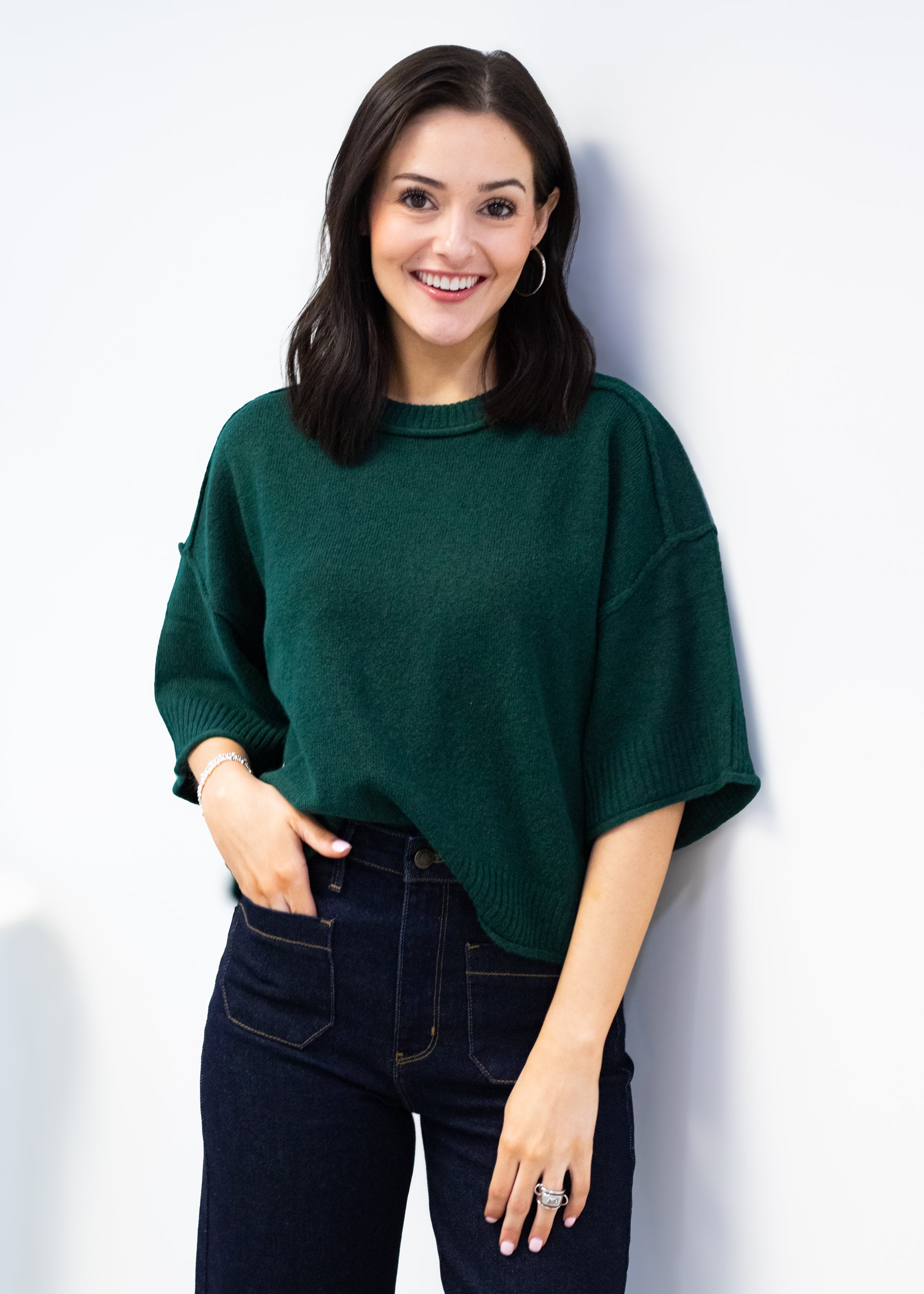 Woman wearing a green sweater and dark jeans against a white background