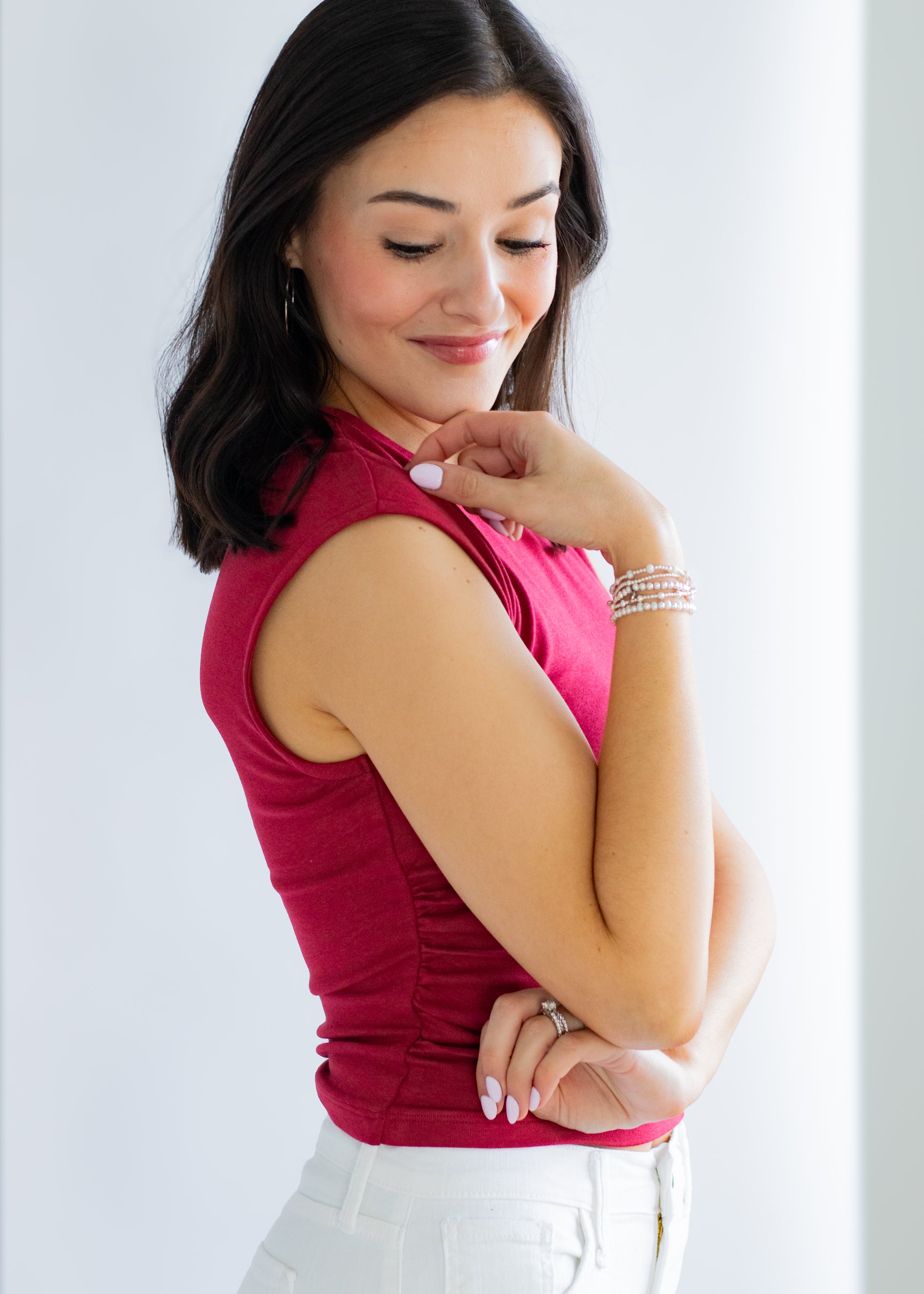 Woman wearing a red sleeveless top and white pants on a light gray background