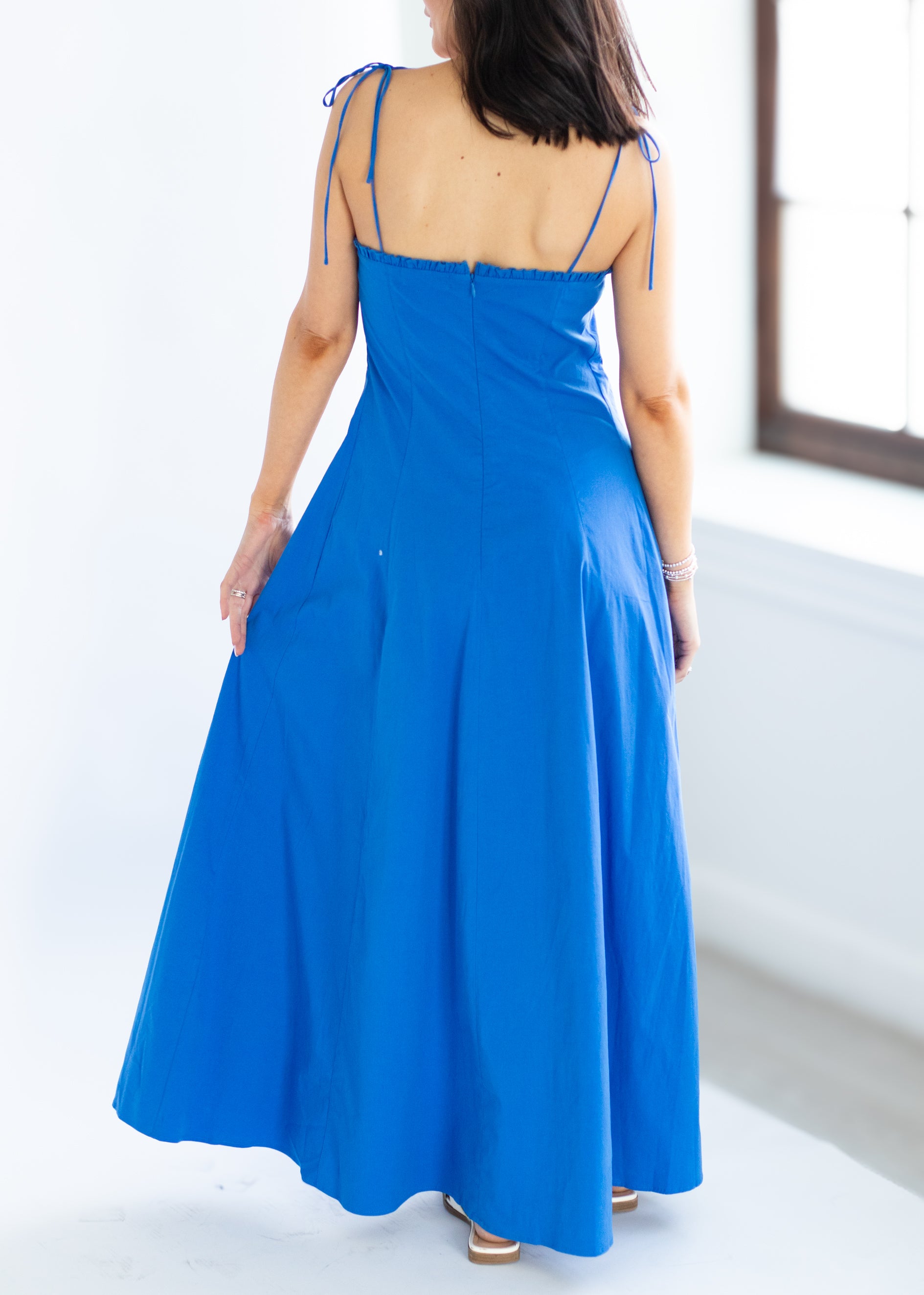 Woman wearing a blue dress with thin straps in a minimal indoor setting