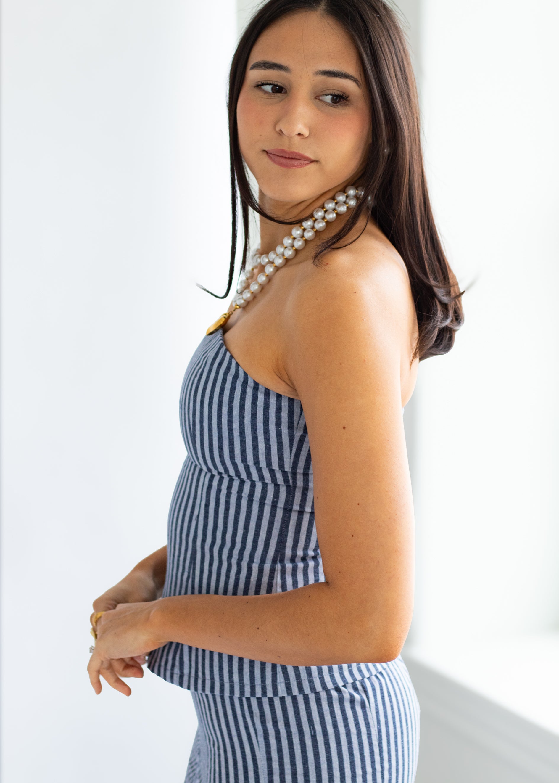 Woman wearing a blue and white striped dress with a pearl necklace against a white background