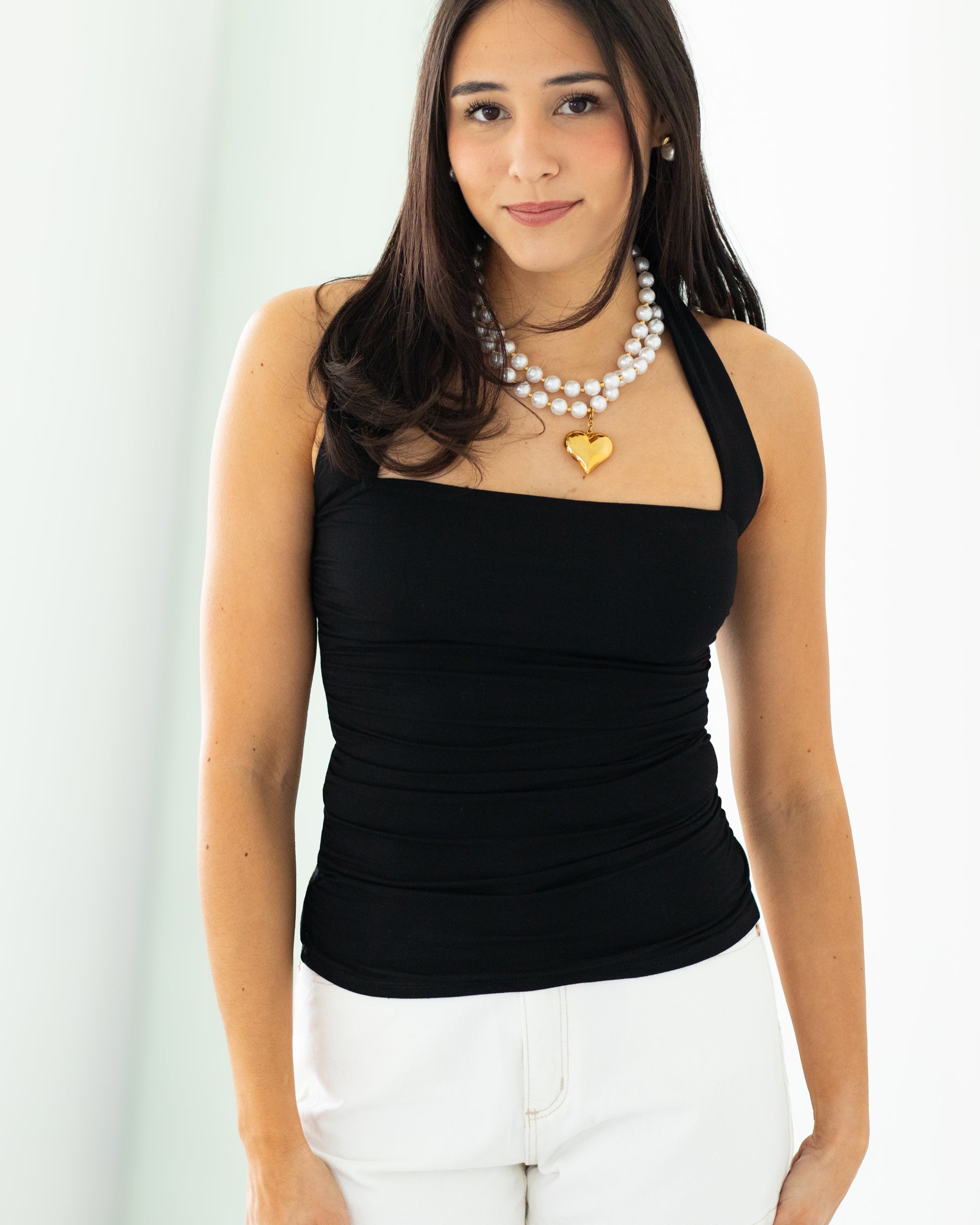 Woman wearing a black top and white shorts with jewelry on a plain background