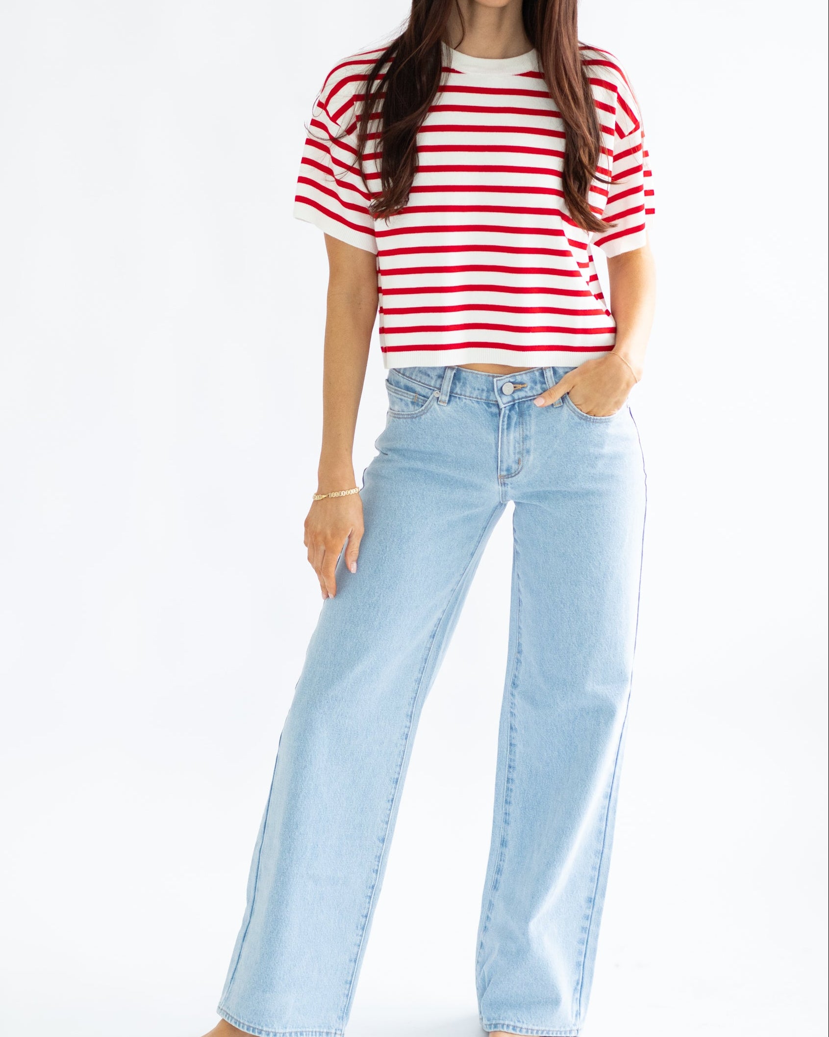 Woman wearing a red and white striped shirt and light blue jeans on a white background