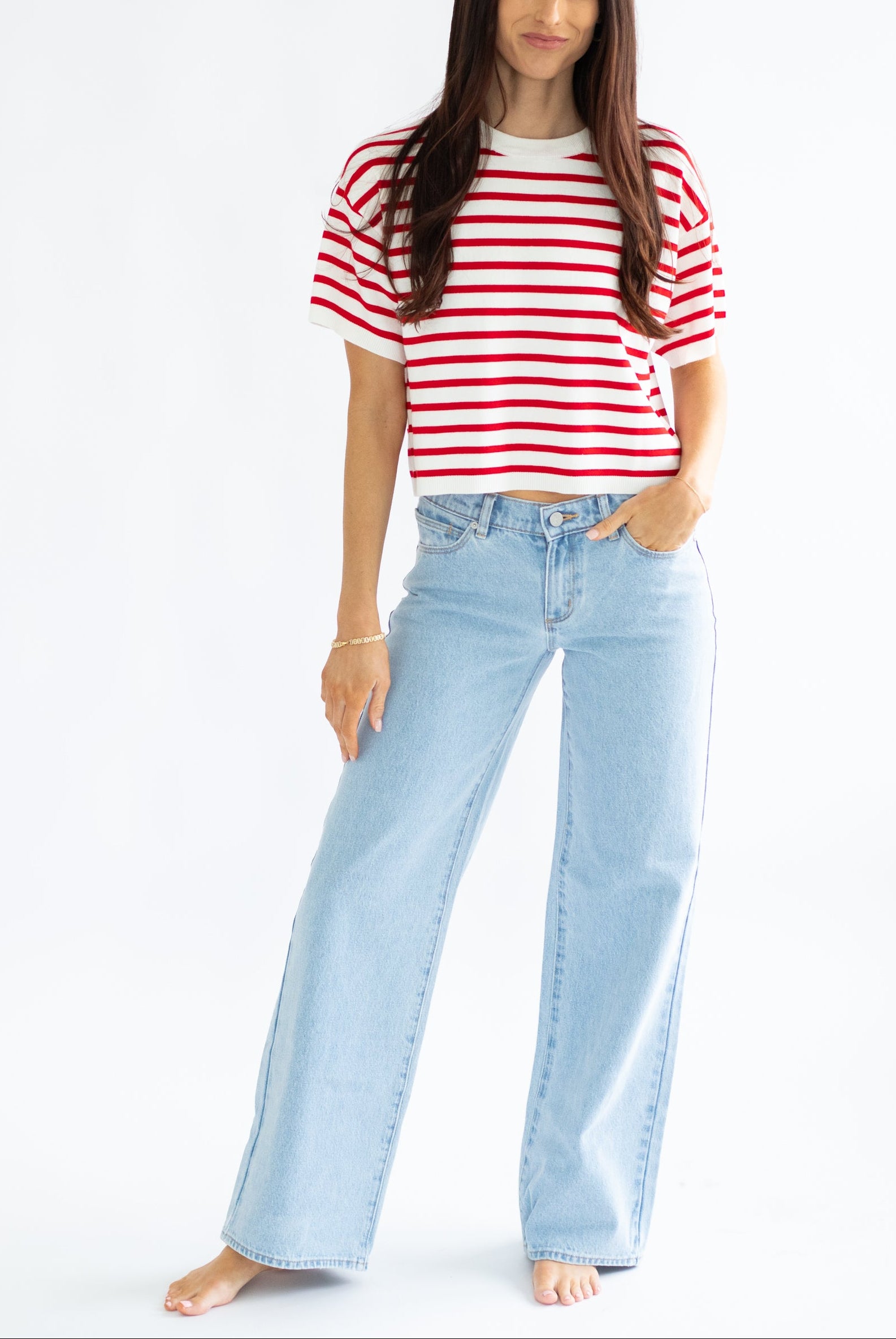 Woman wearing a red and white striped shirt and light blue jeans on a white background