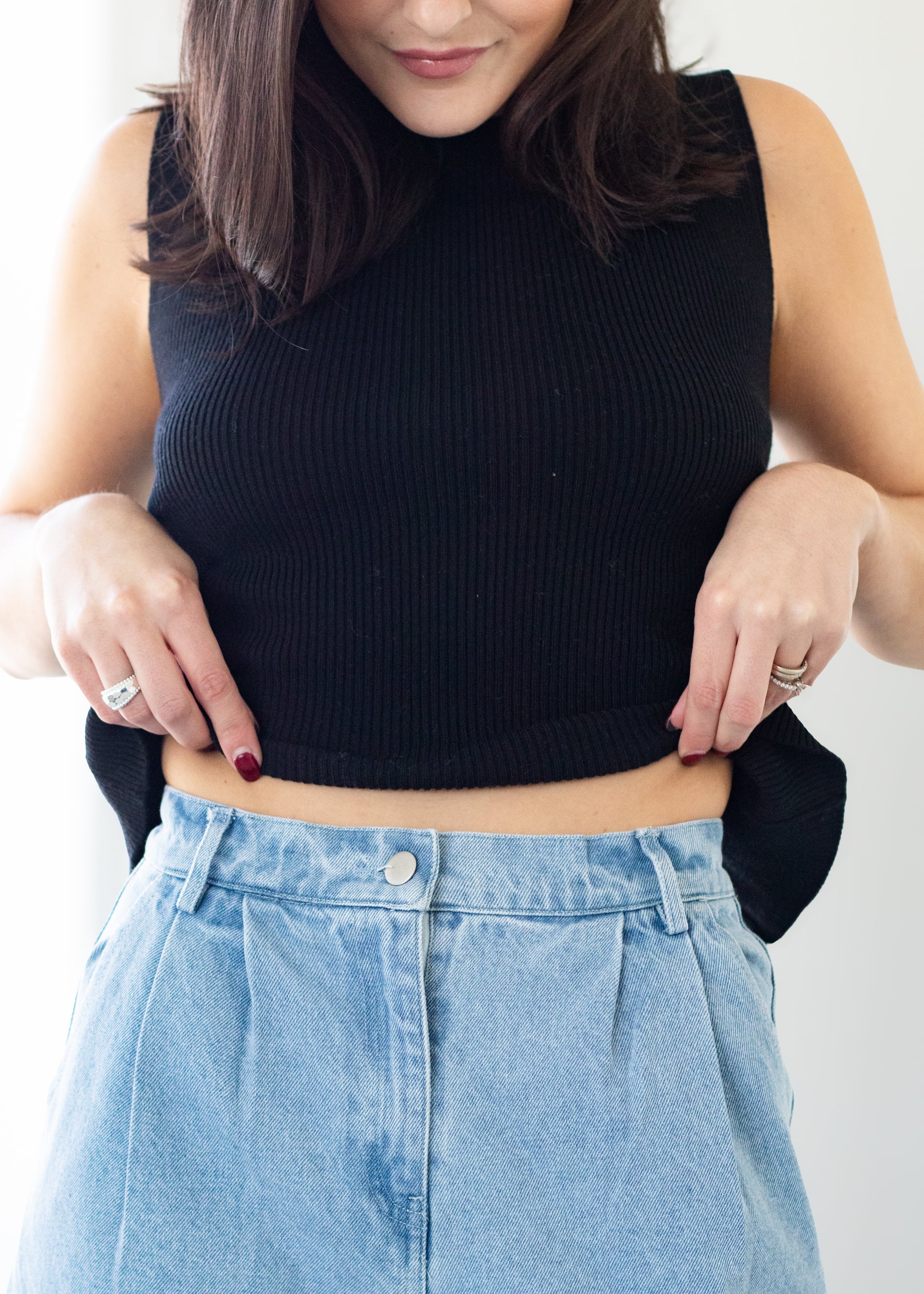 Person wearing a black sleeveless top and blue jeans on a white background