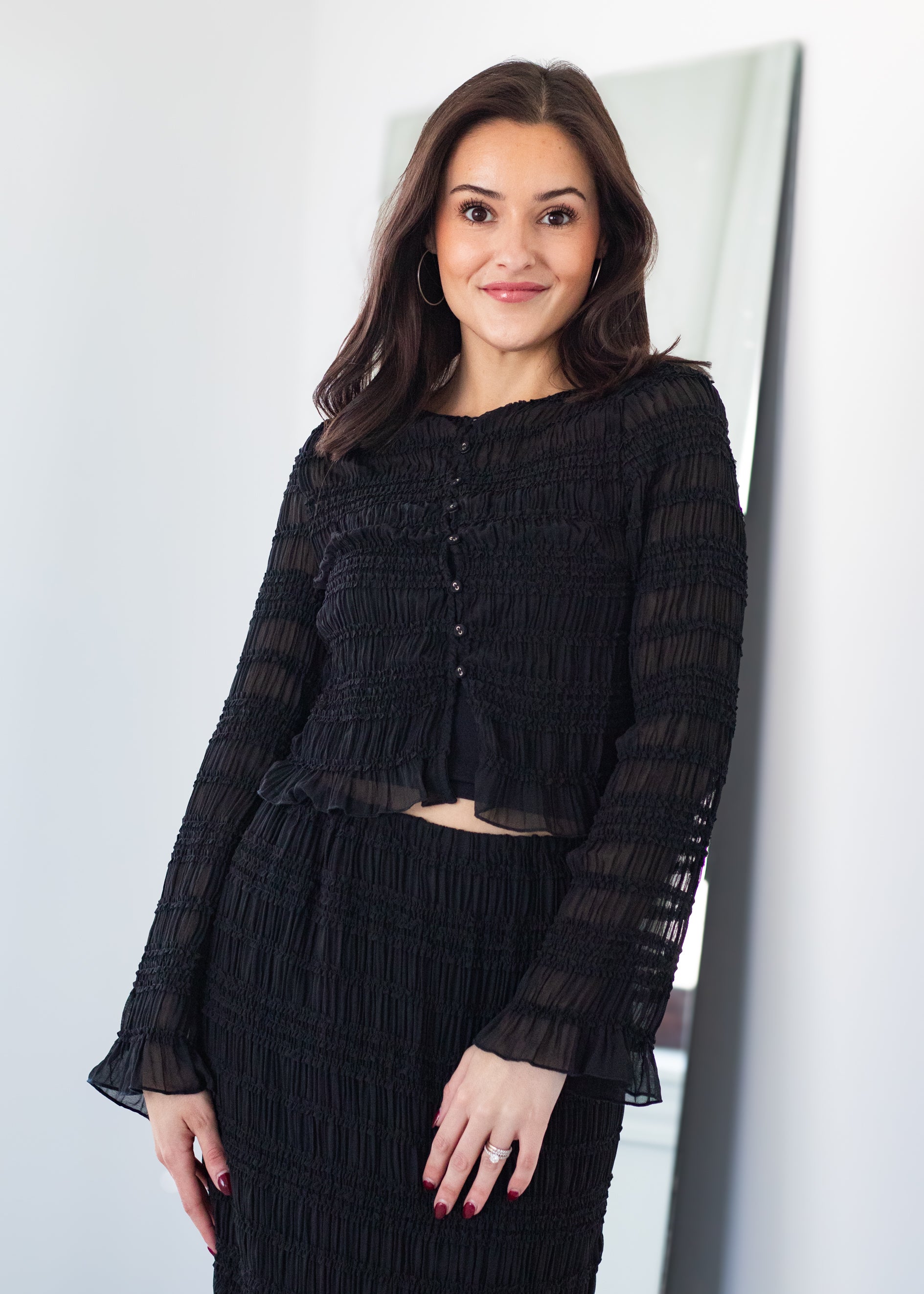 Woman wearing a black outfit standing against a white wall.