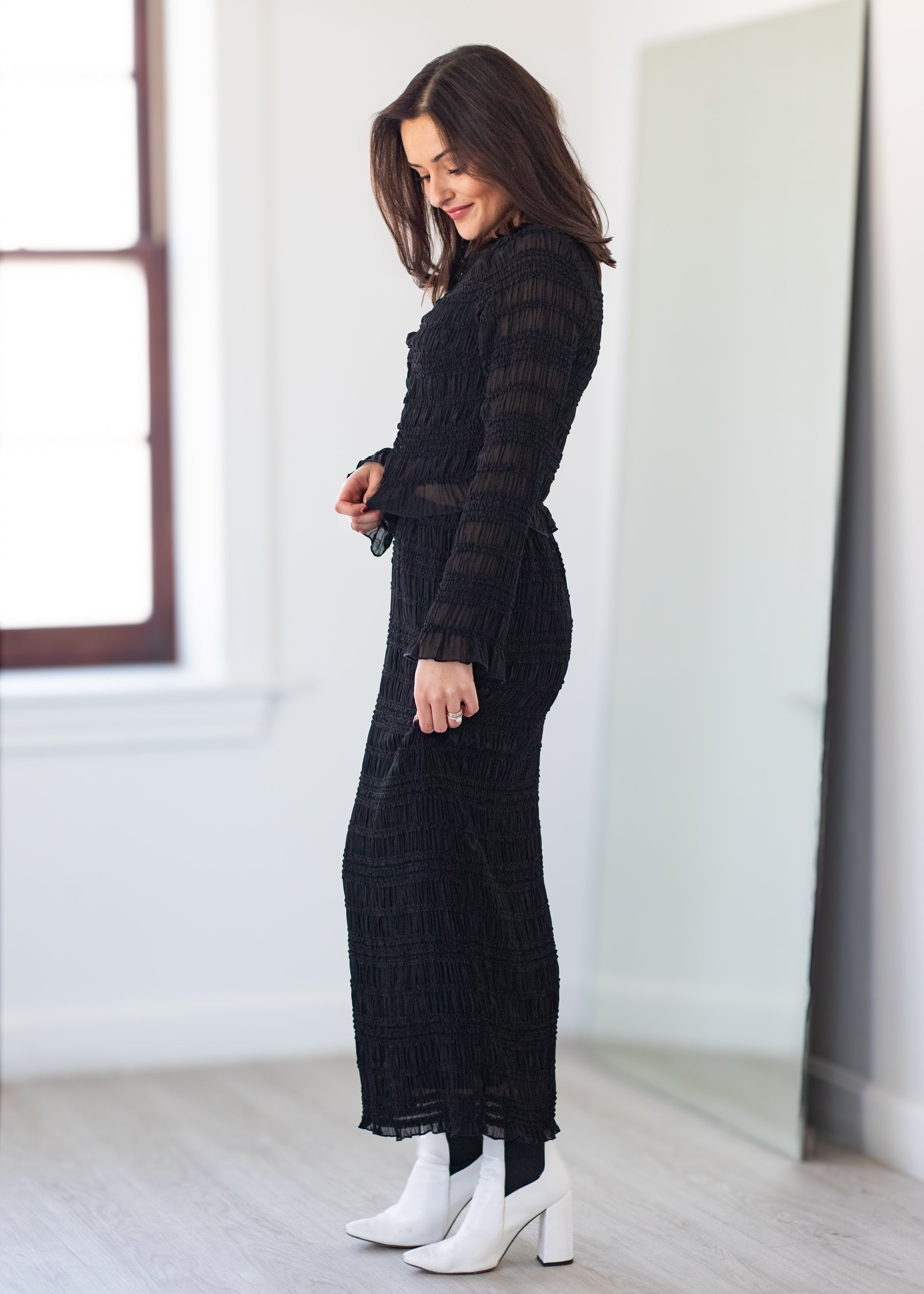 Woman wearing a black dress with white boots in a minimalistic room.