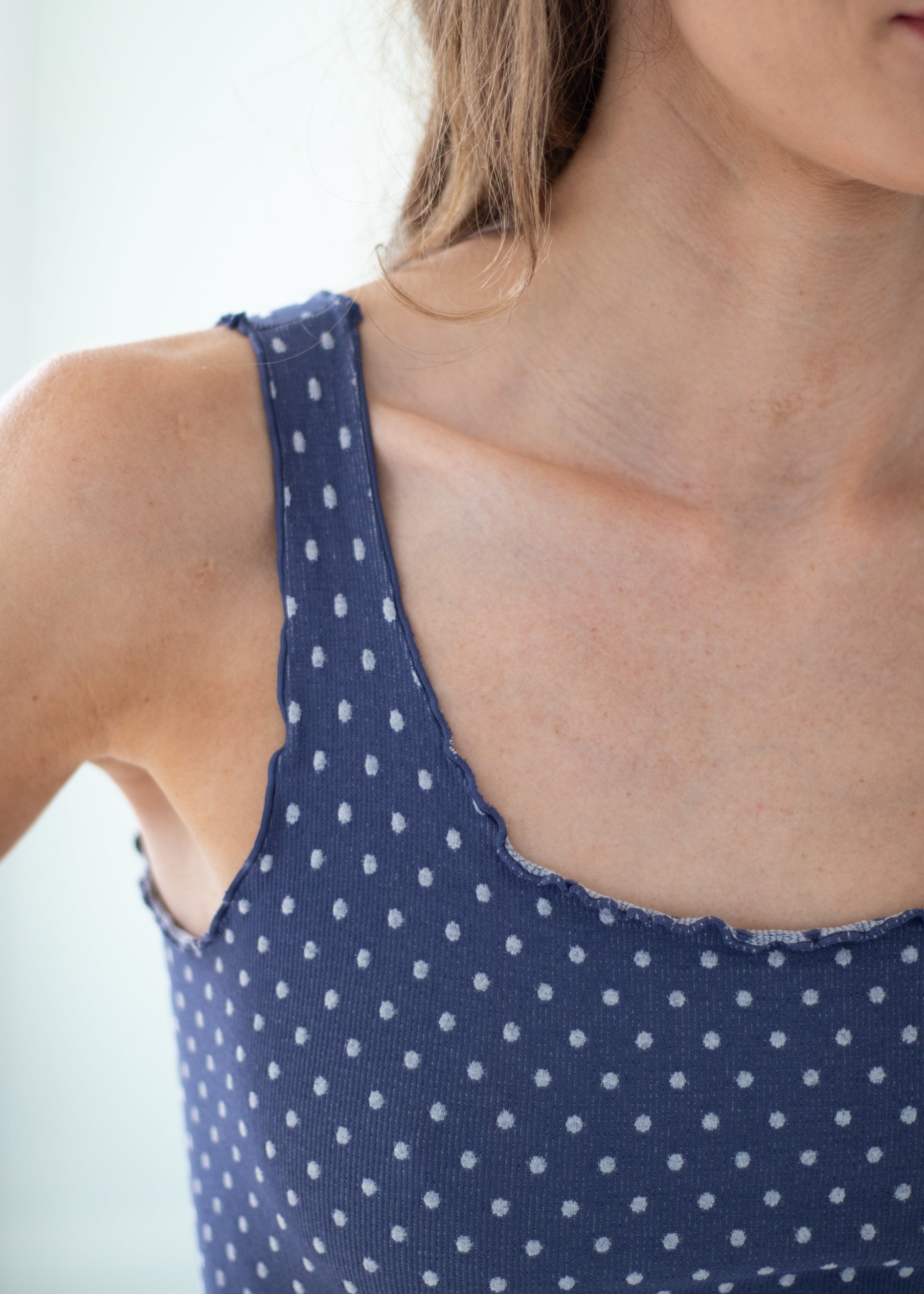Close-up of a person wearing a navy blue ribbed tank top with a white polka dot pattern and a scalloped neckline.