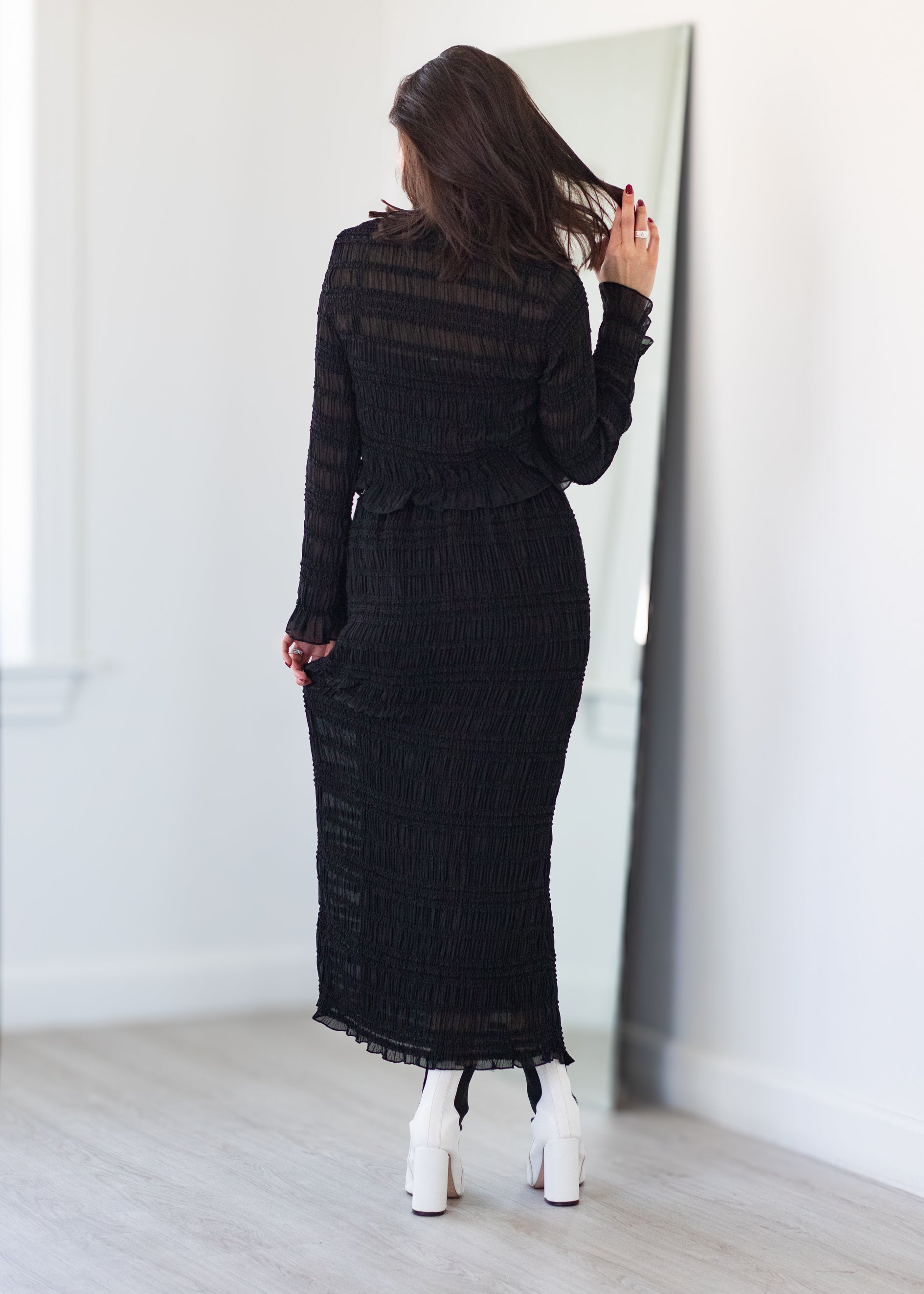 Woman wearing a black dress standing in front of a mirror.