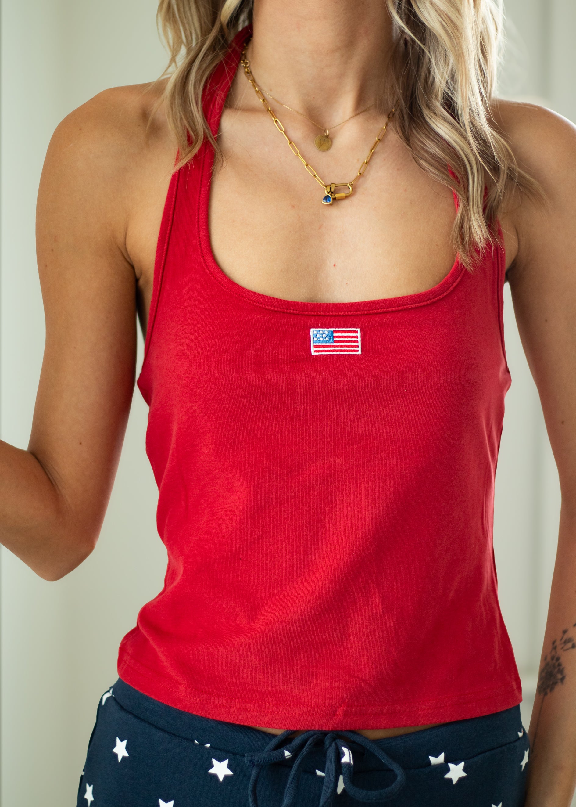 Red tank top with an American flag patch worn by a person against a neutral background