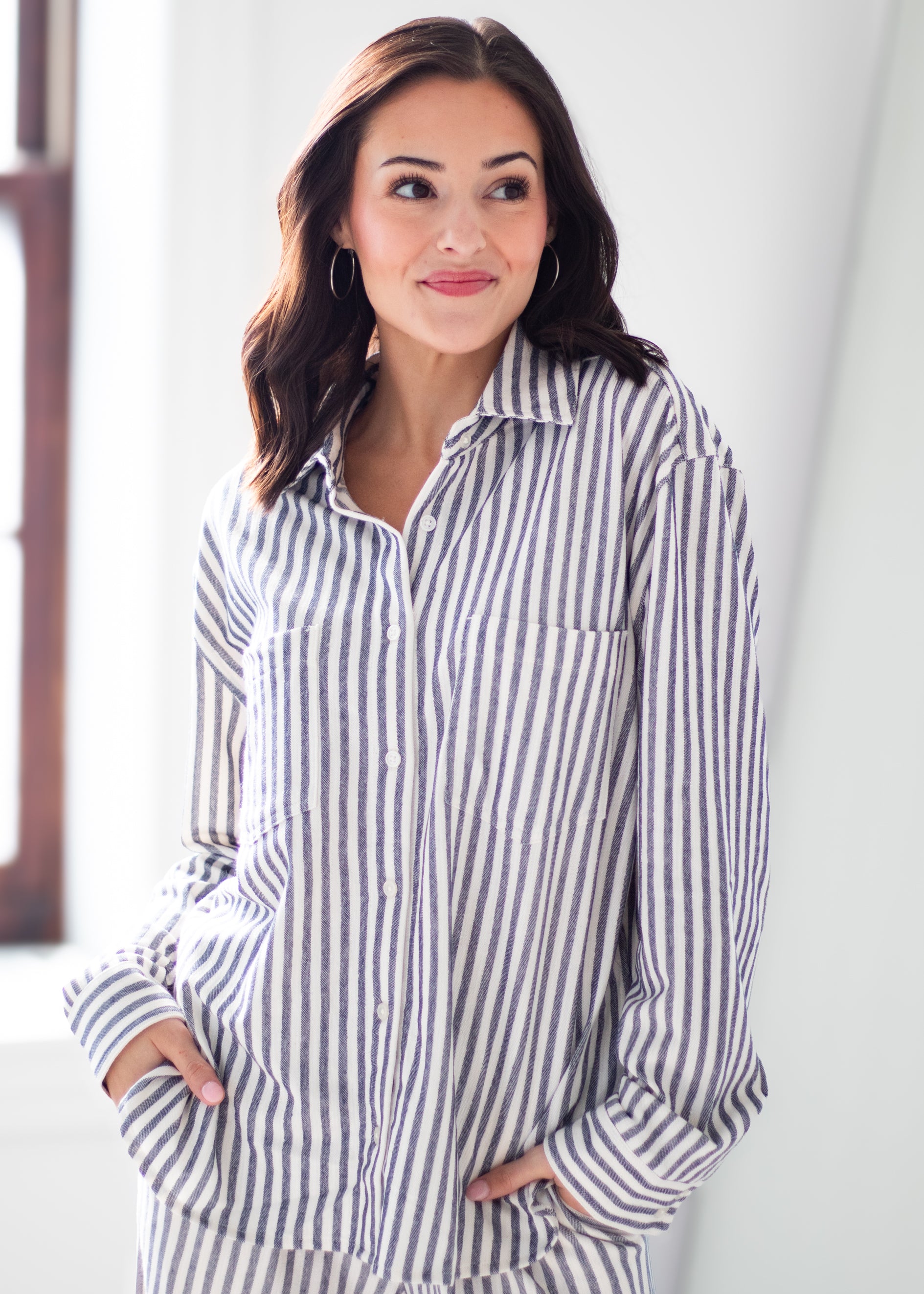 A woman wearing a long-sleeve button-up shirt with vertical navy and white stripes, standing in a brightly lit indoor setting.