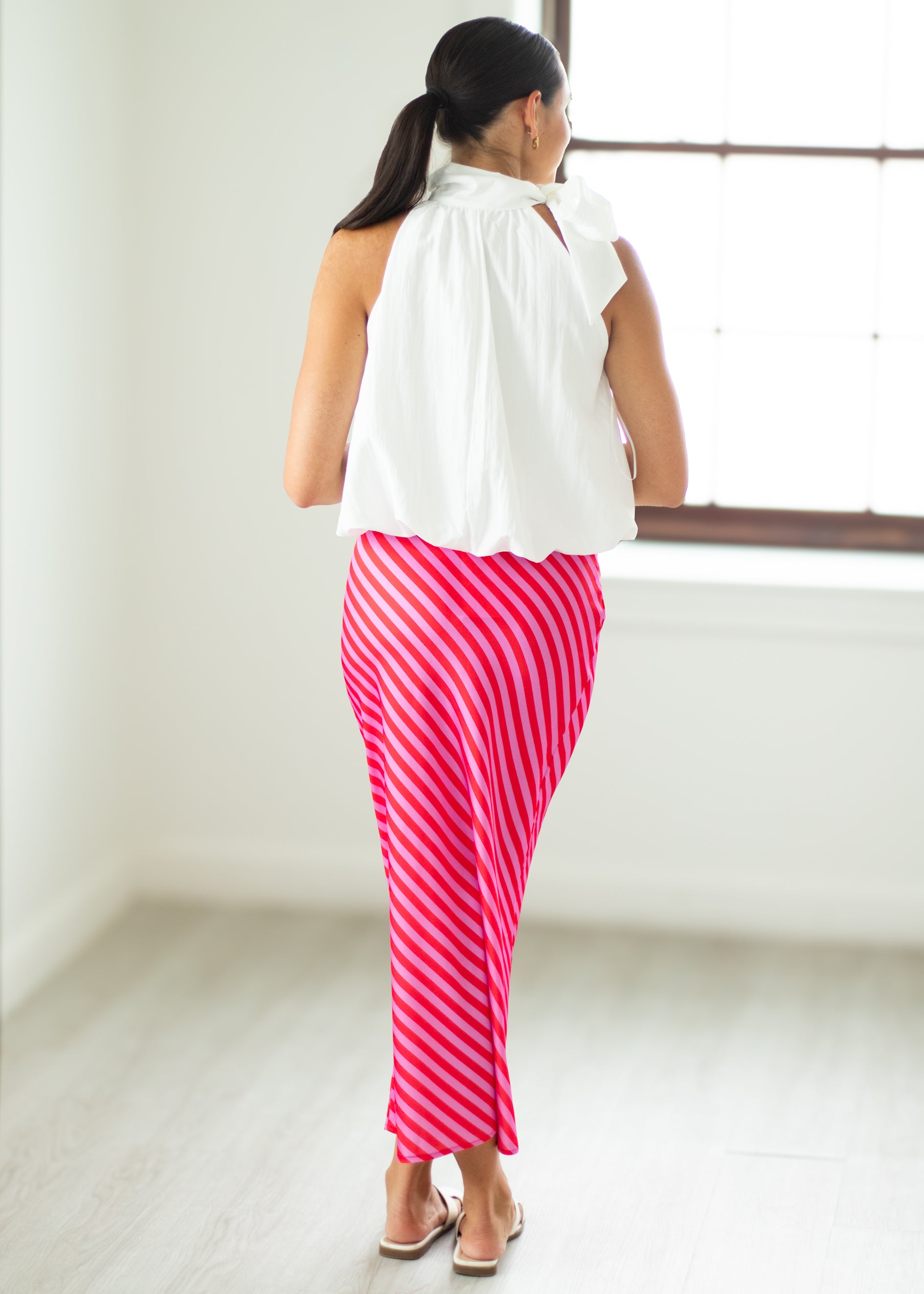 Woman wearing a white top and pink striped pants in a minimal indoor setting