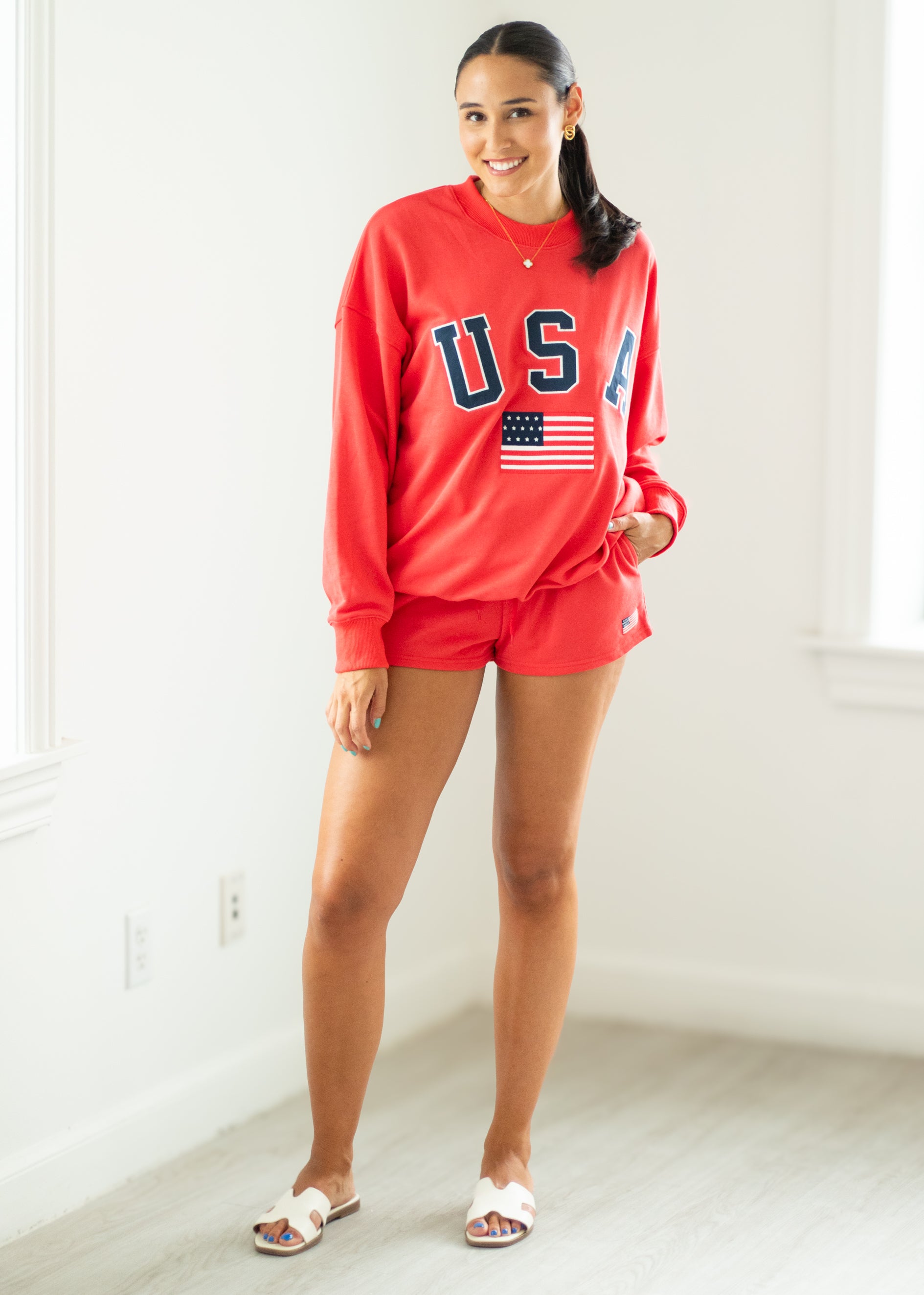 Woman wearing a red 'US' sweatshirt and shorts in a room with white walls.